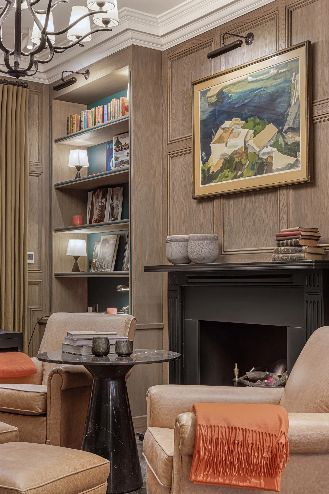 Framed painting above a fireplace beside library shelving — AKC Asset Management, part of AKC Group.