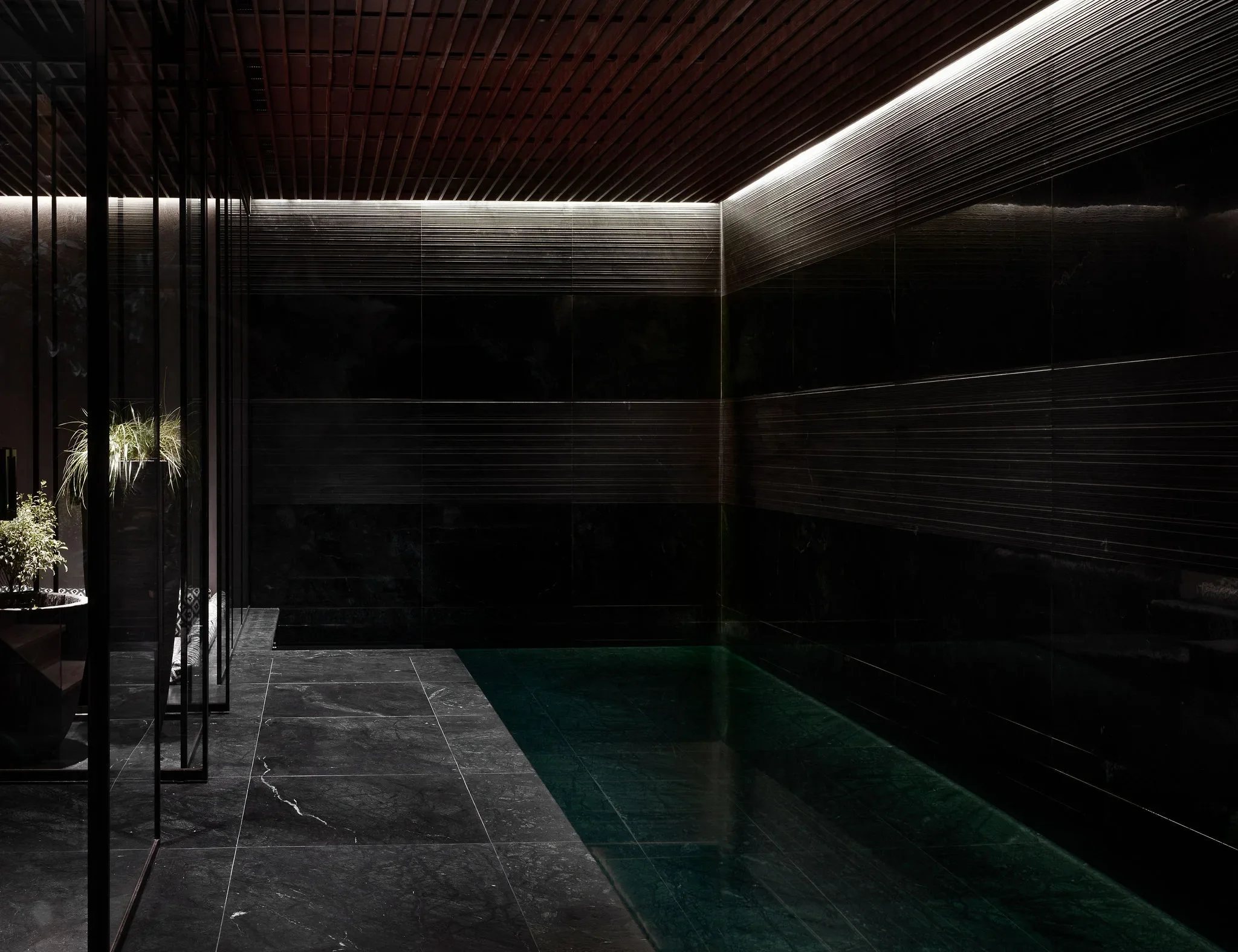 Dark-tiled indoor pool with concealed ceiling lighting — AKC Asset Management real estate, part of AKC Group.