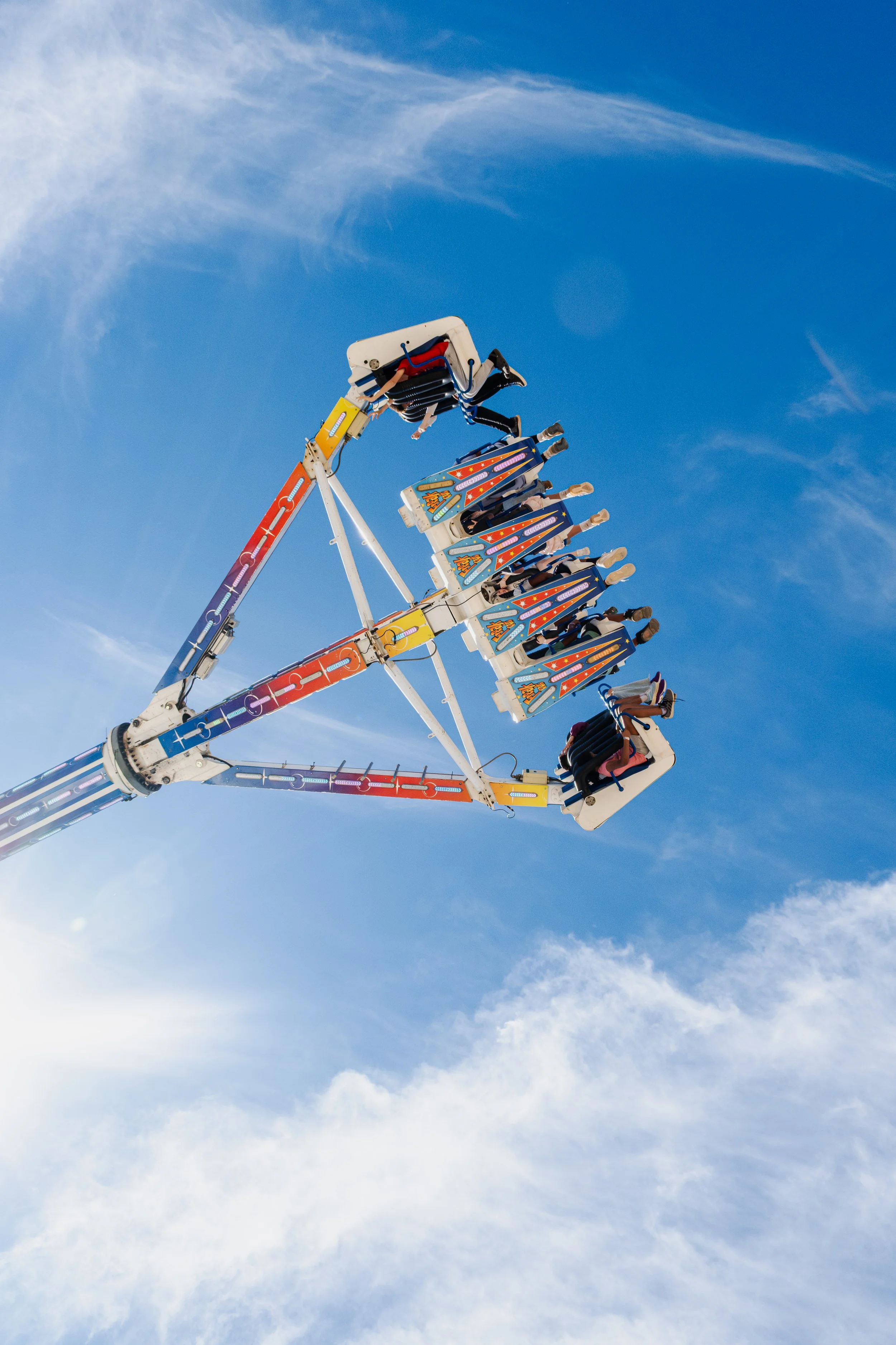 Ferris wheel with people riding, set against a bright blue sky with some wispy clouds.
