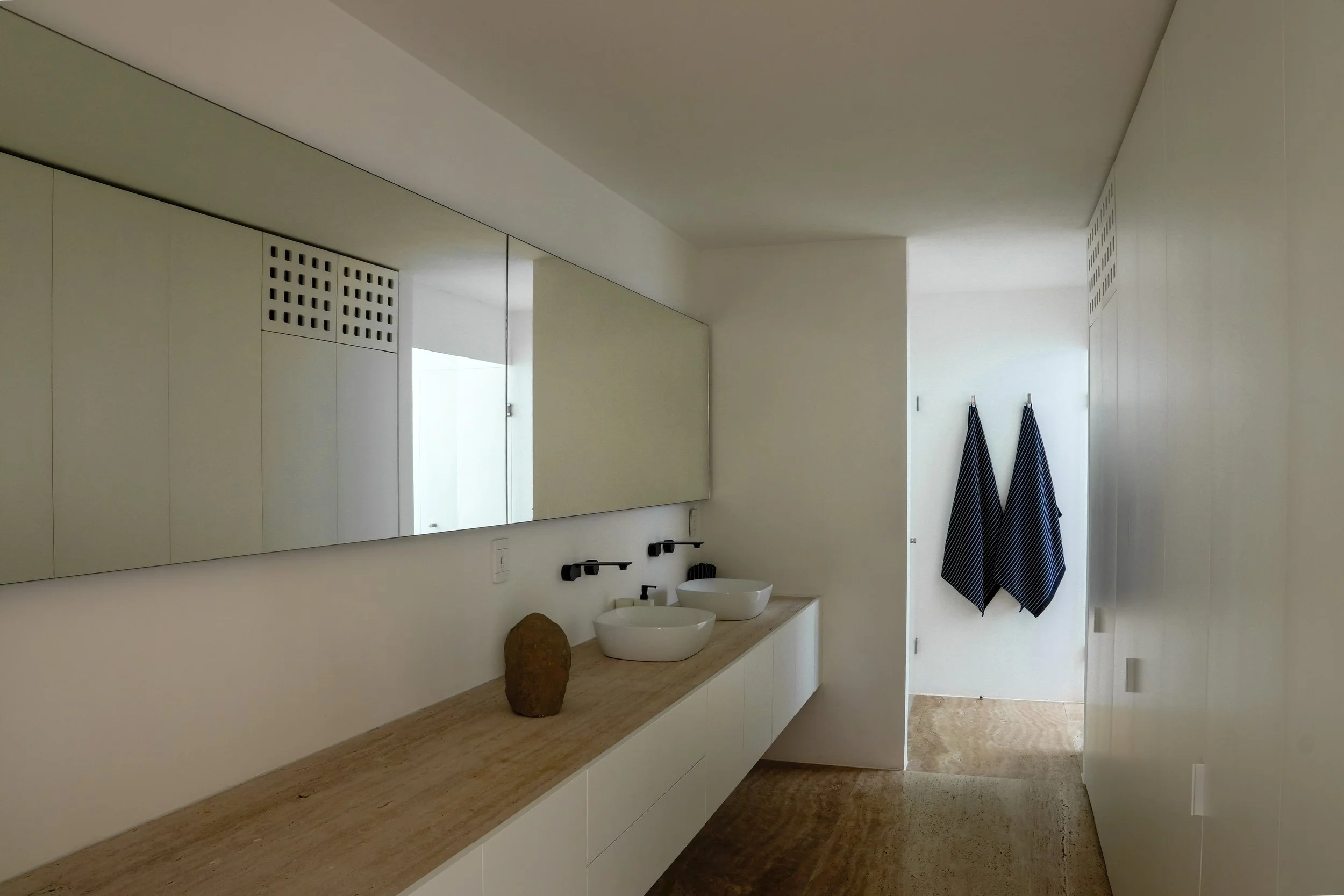 Modern bathroom with white cabinetry, a large mirror, two vessel sinks, and two black towels hanging on the wall.