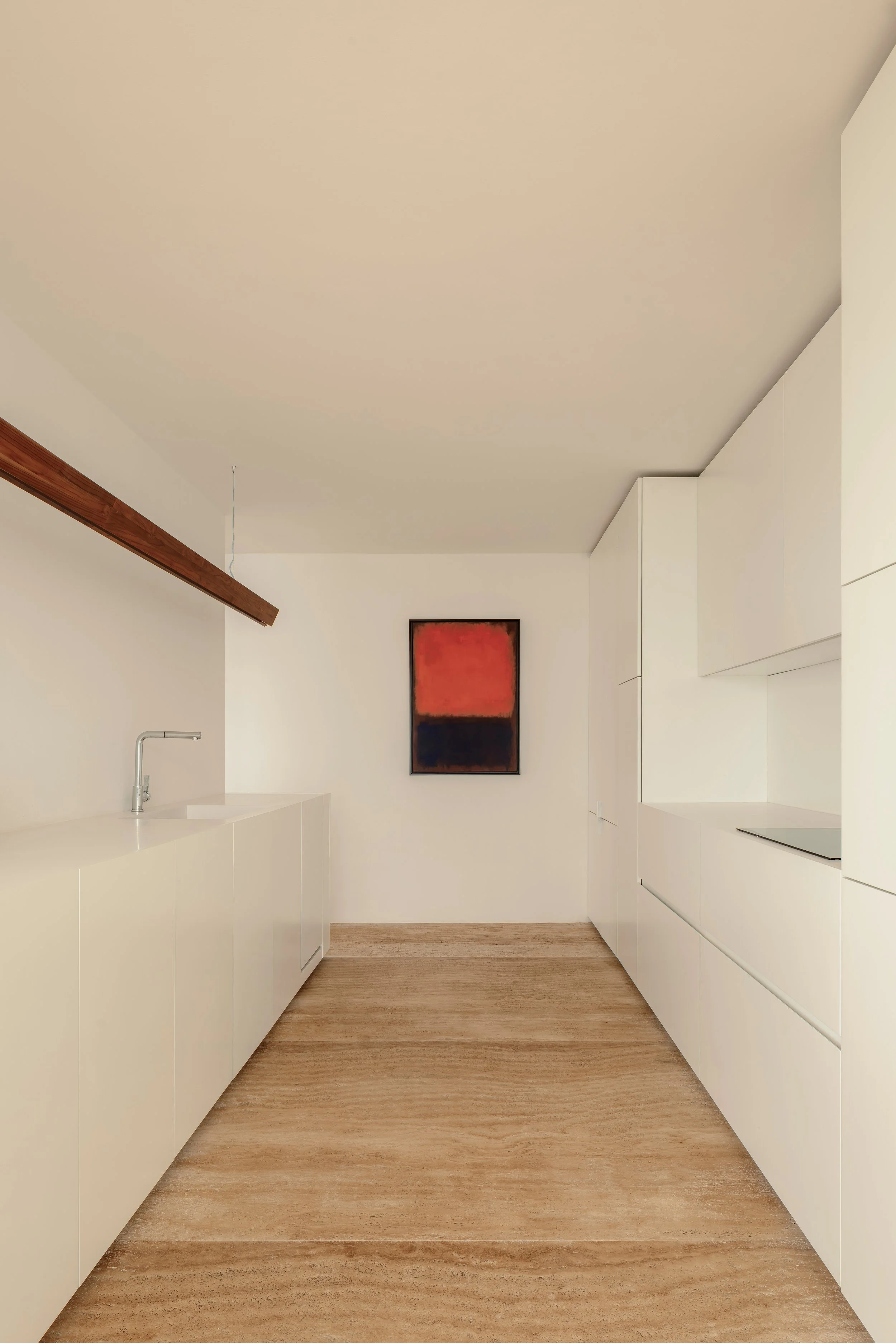 Minimalist modern kitchen with white cabinetry, a small sink, artwork on the wall, and light wood flooring.