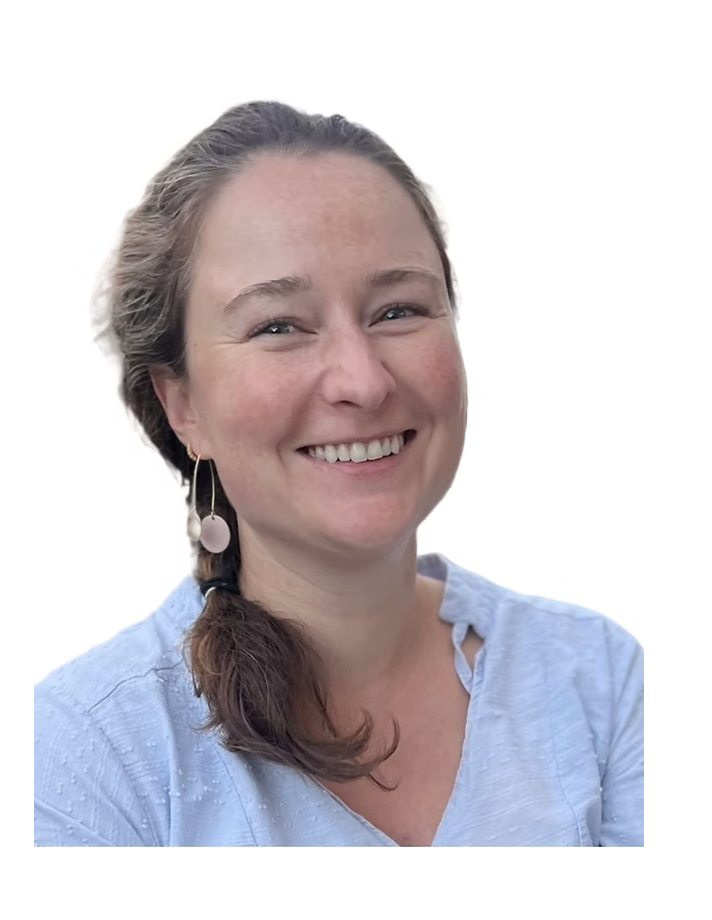 A woman with light brown hair in a braid, wearing a light blue blouse and a dangle earring, smiling against a plain white background.