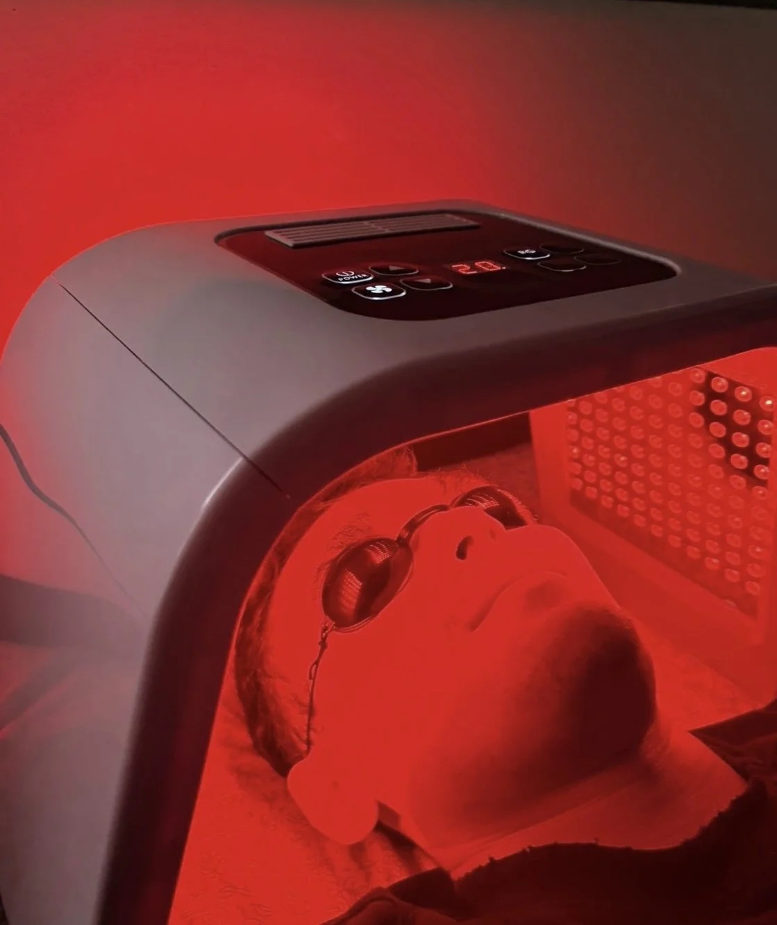 A person undergoing a red light therapy session in a specialized device, with their face illuminated by red LED lights.