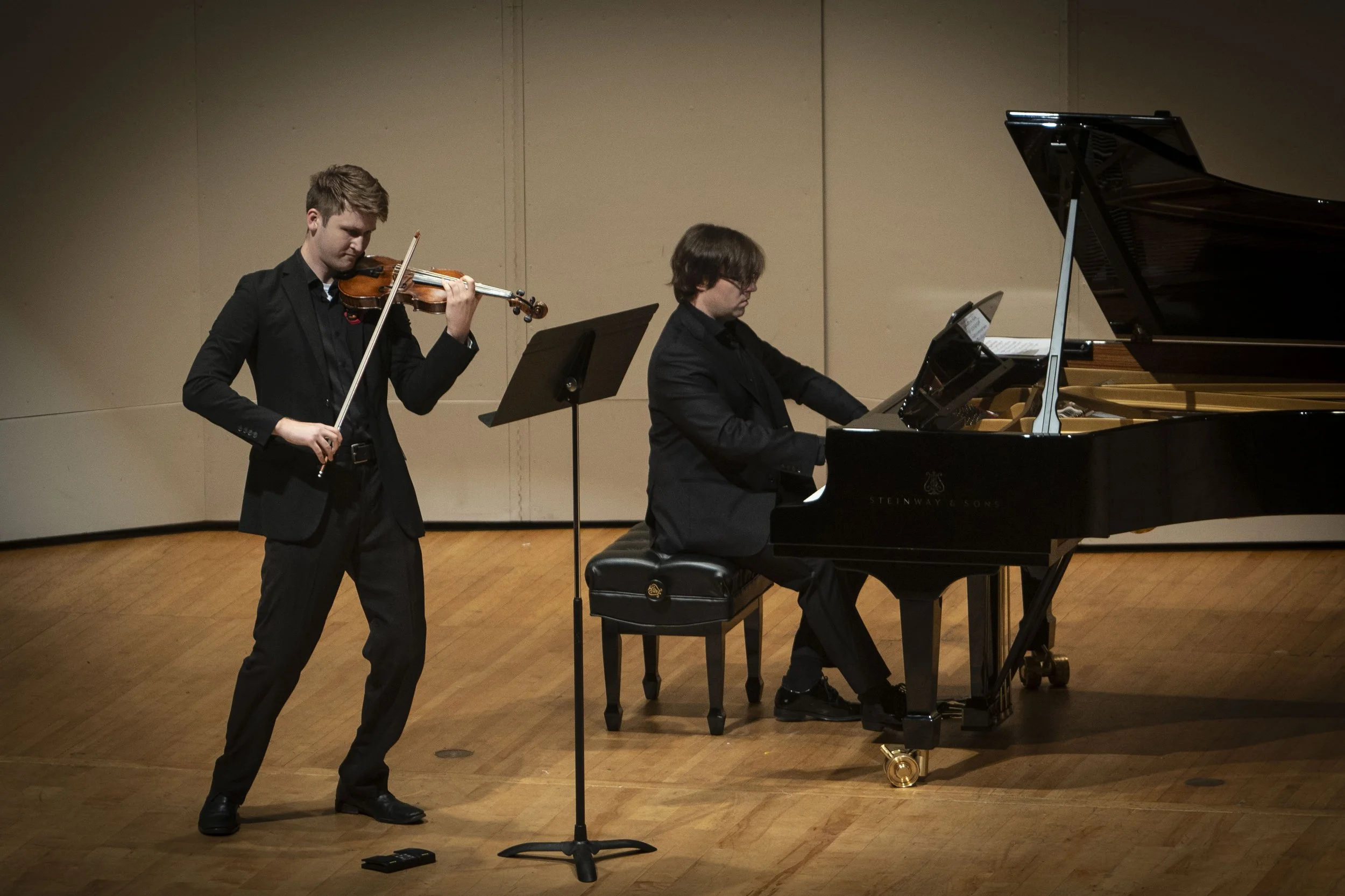 Two musicians performing on stage: one playing the violin and the other playing the grand piano.