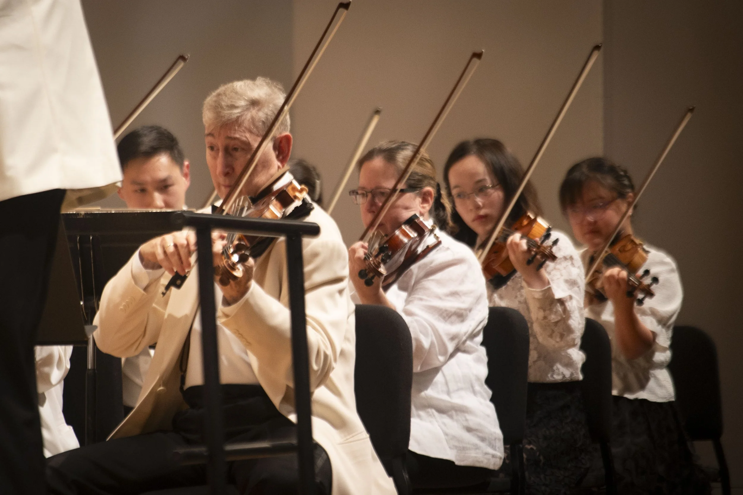 Randall Weiss and other artist-faculty playing violins during a performance, seated in a row, with music stands in front of them, focused on their music.