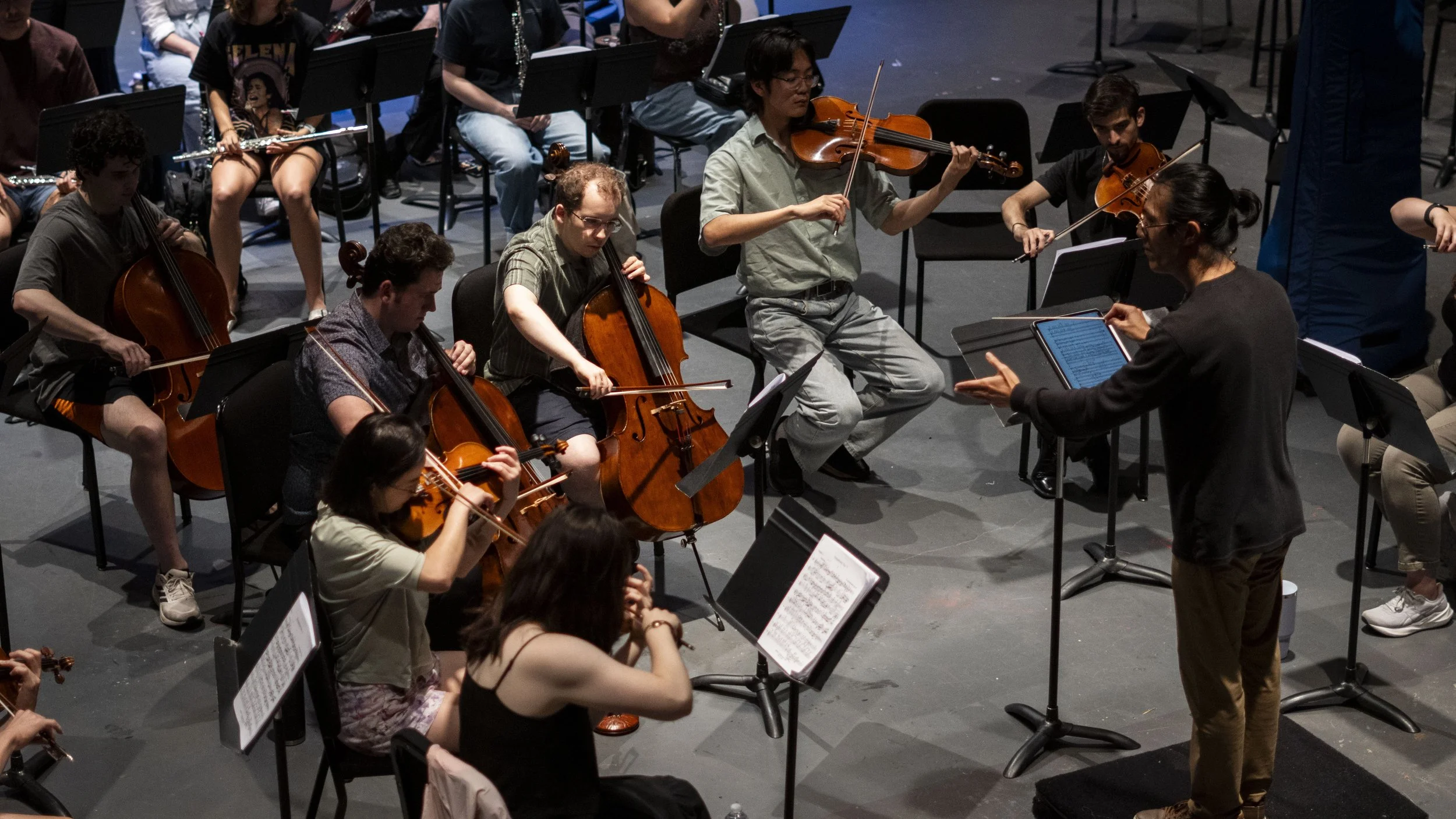 Orchestra rehearsal with musicians playing string and wind instruments with a conductor leading the ensemble.