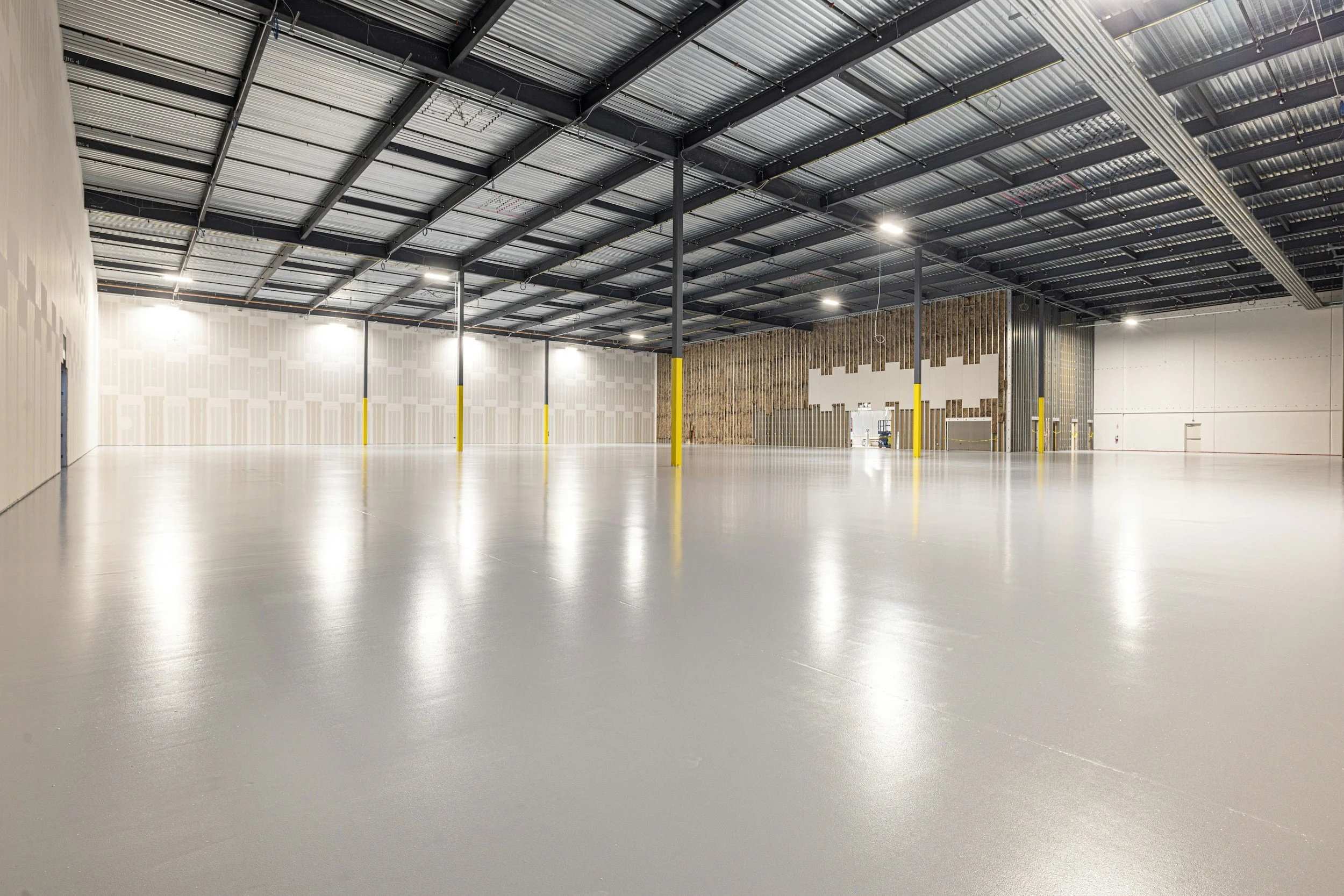 Empty indoor warehouse with concrete floor, high metal ceiling, and yellow safety poles.
