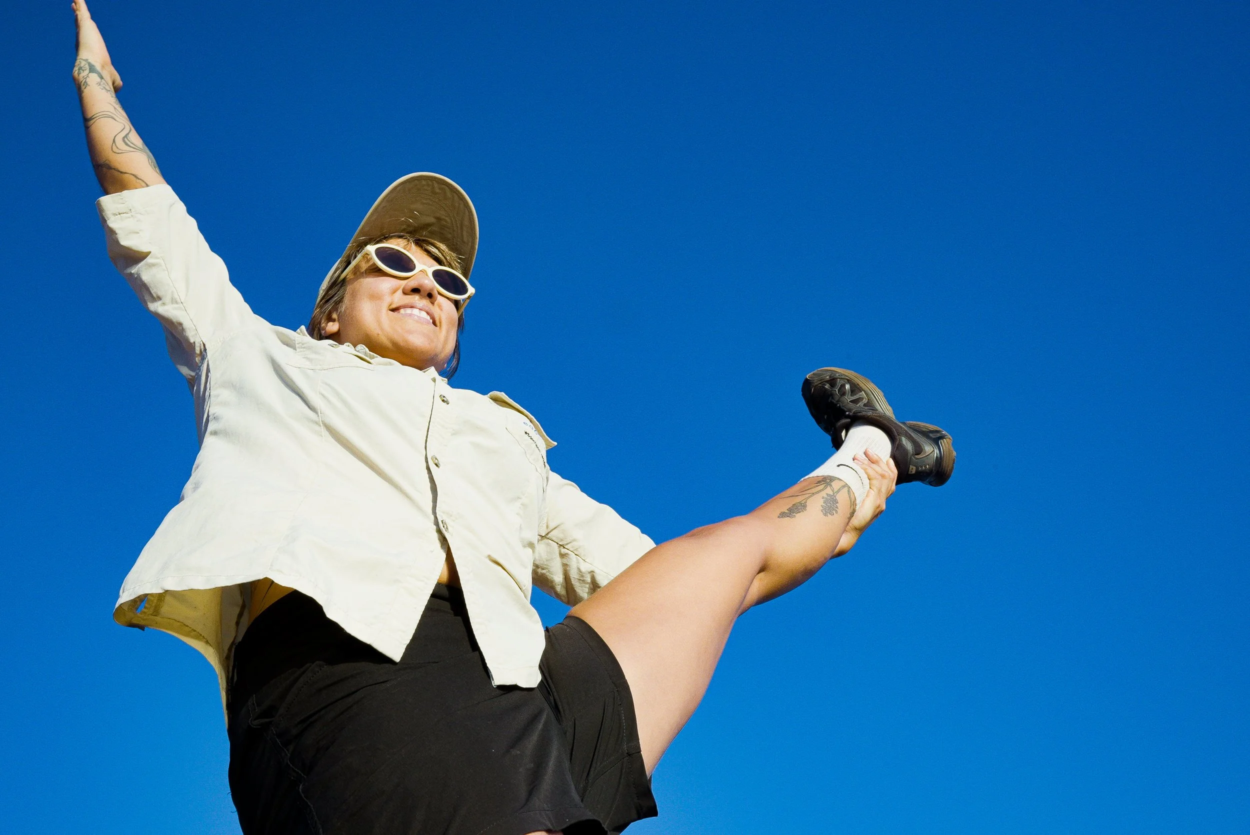 A woman with sunglasses and a wide-brim hat being lifted by another person, against a clear blue sky.