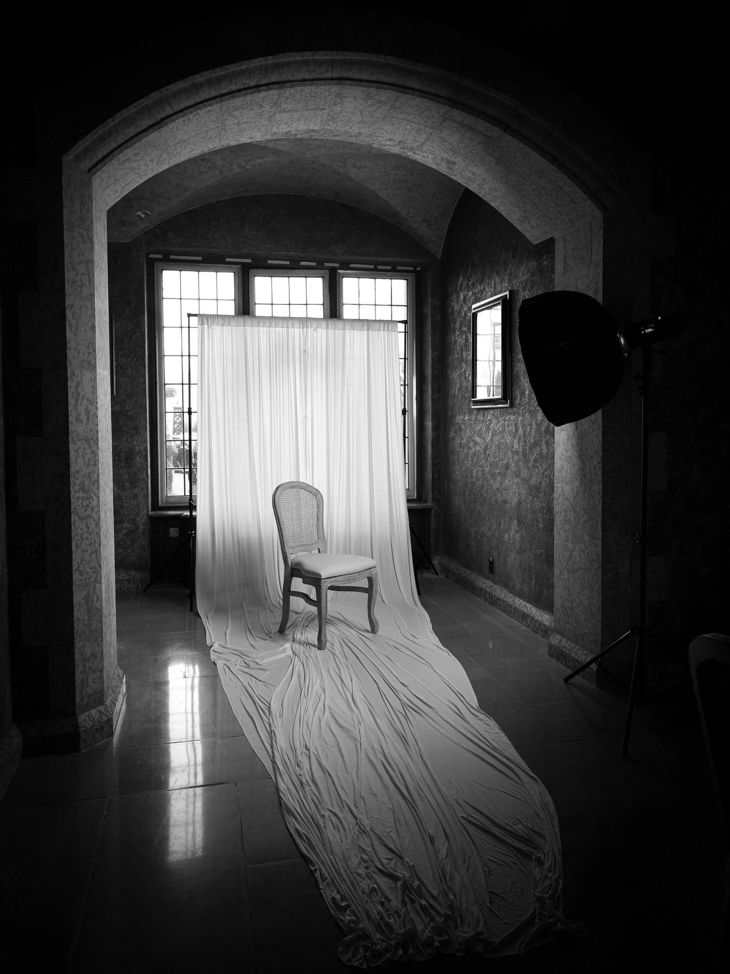 a mobile portrait studio set with a simple white draped backdrop, decorative chair and lighting elements under a stone archway