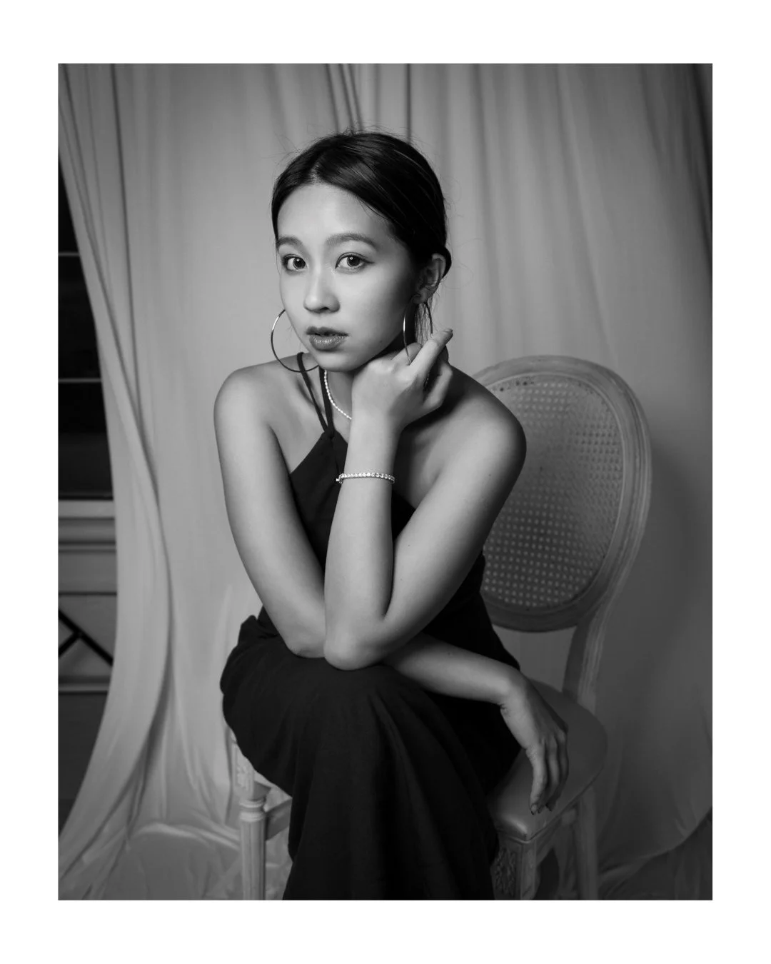 Black and white portrait of a young woman in hoop earrings, seated with her chin on her hand