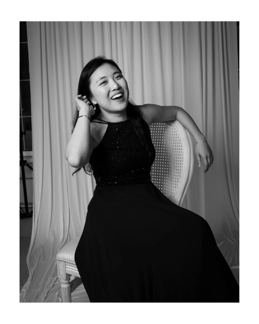 Black and white portrait of a laughing woman in a sleeveless black dress seated on a chair