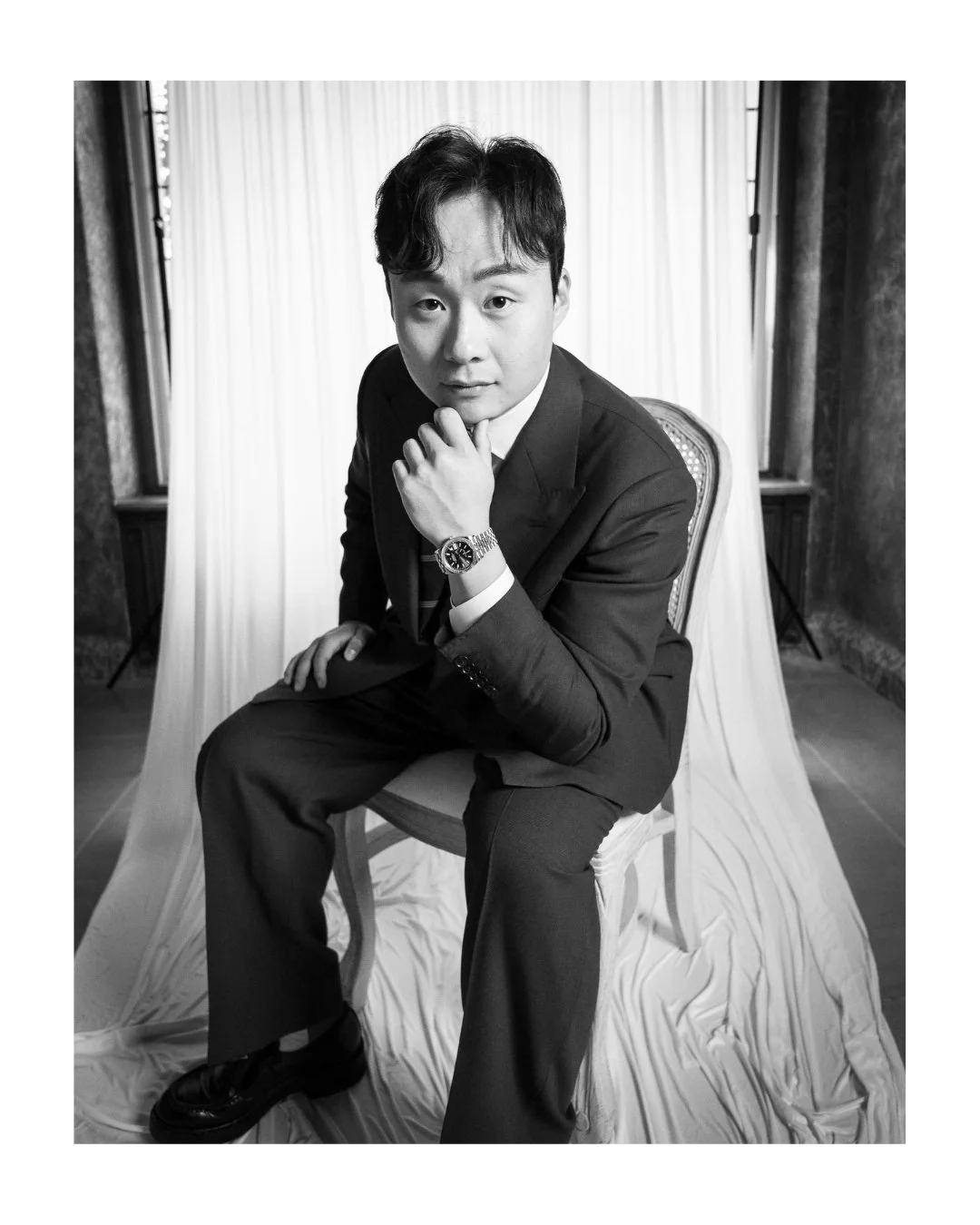 Black and white portrait of a young man in a suit, seated chin resting on his hand