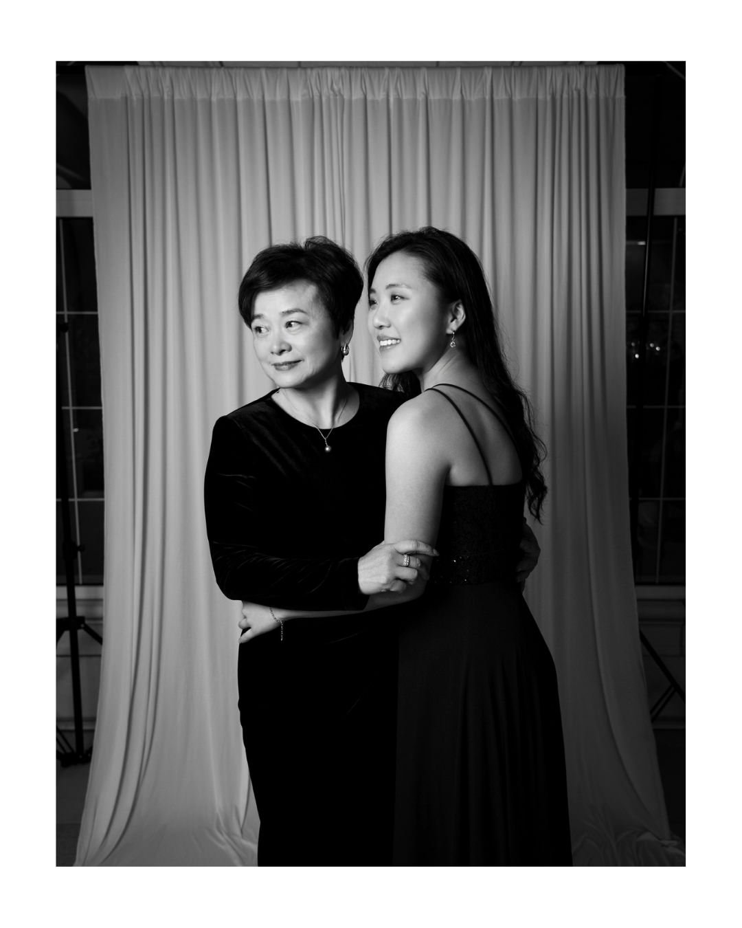Black and white portrait of two smiling women, one older and one younger, in front of a draped backdrop