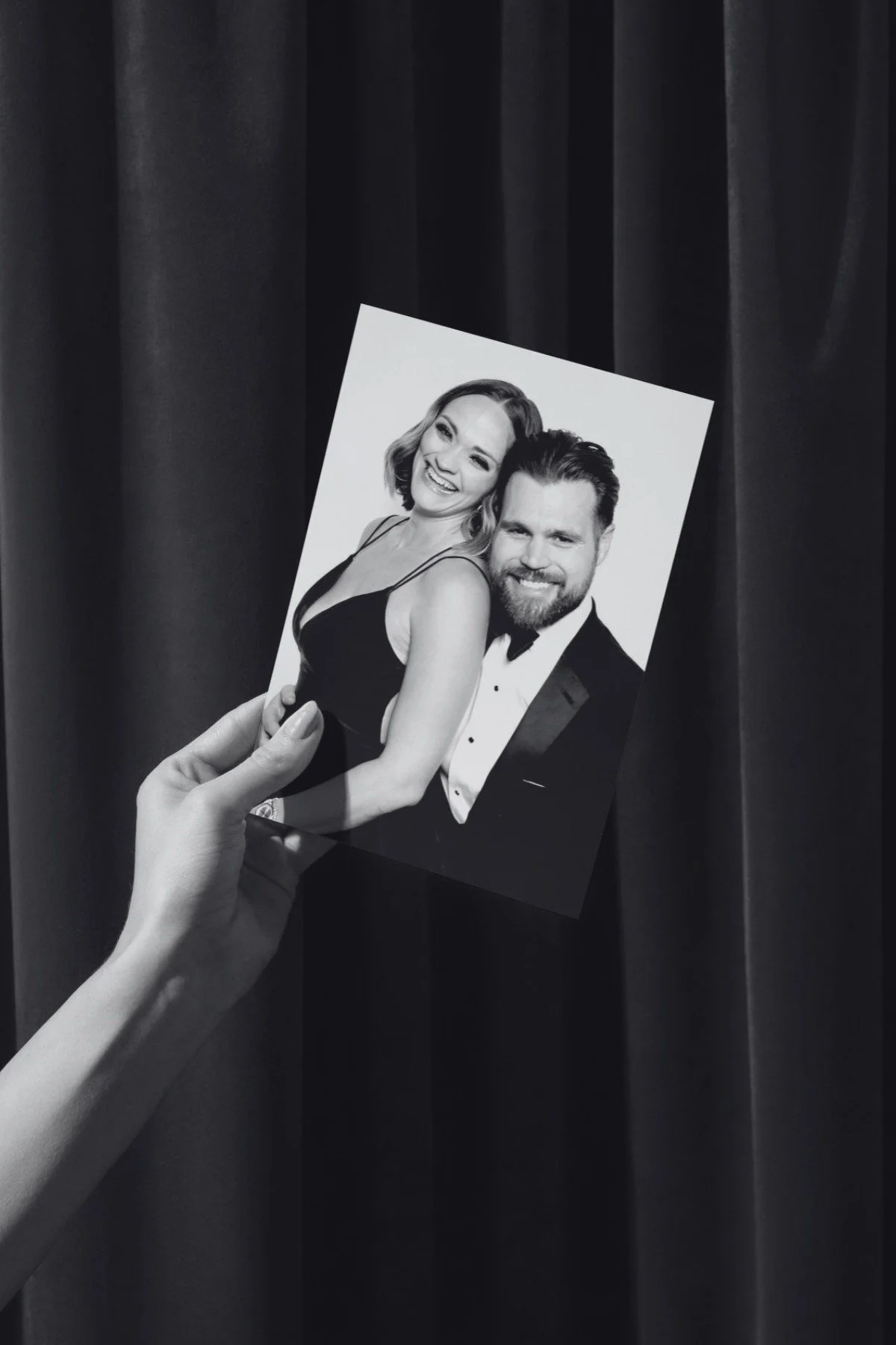 Hand holding a black and white 4x6 print of a smiling couple in formal wear from the portrait station