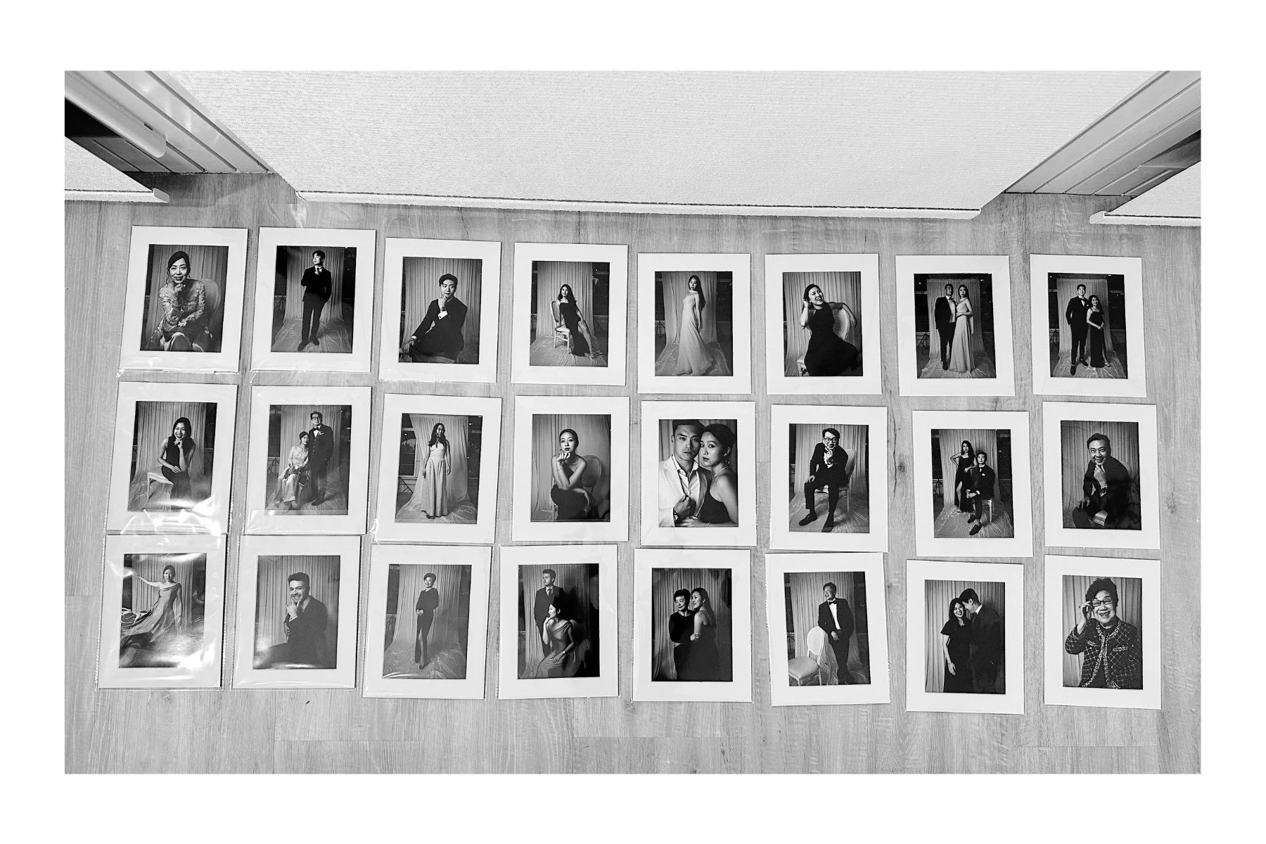 Collection of black and white portrait photographs of a diverse group of wedding guests, arranged in rows on a wooden floor for display.