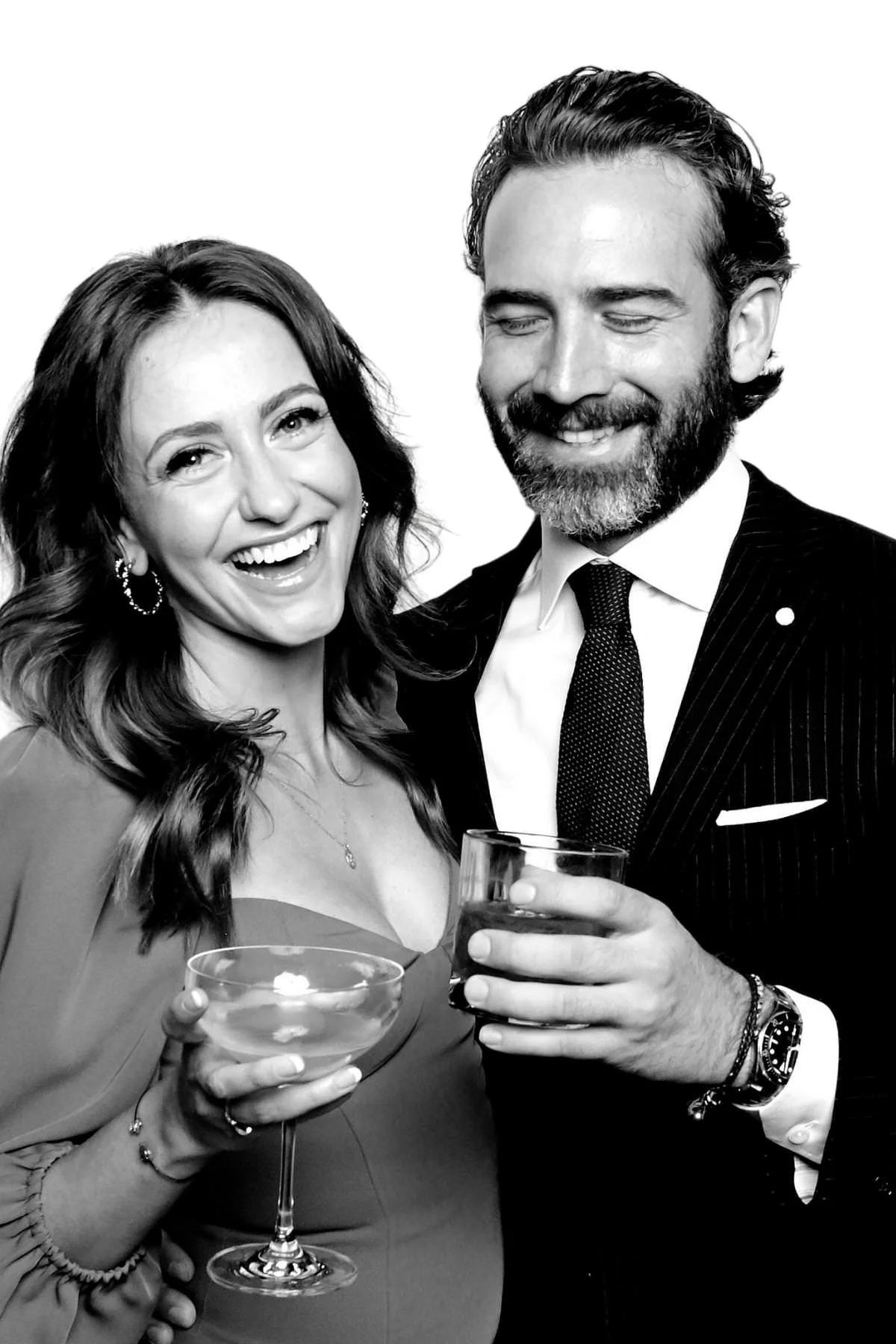 Laughing couple holding cocktails, she in hoop earrings and he in a pinstripe suit, black and white portrait