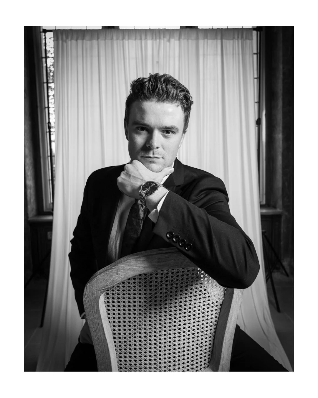 Black and white portrait of a young man in a suit seated with his chin on his hand