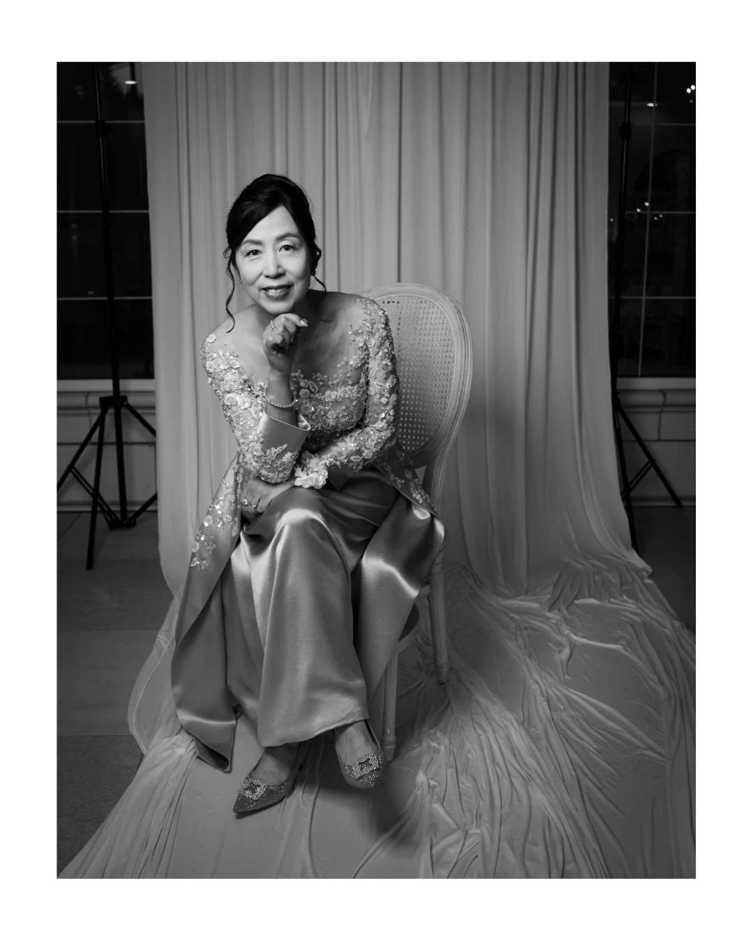 Smiling woman in an embroidered satin outfit seated on a cane-back chair in a draped portrait set at Archway Manor