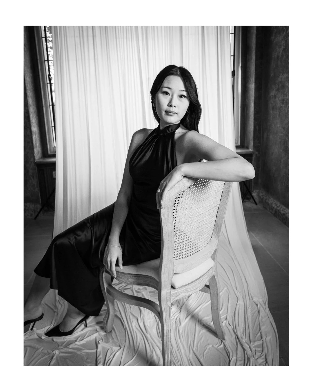 Black and white portrait of a wedding guest in a dark dress, seated with her arm on the chair back