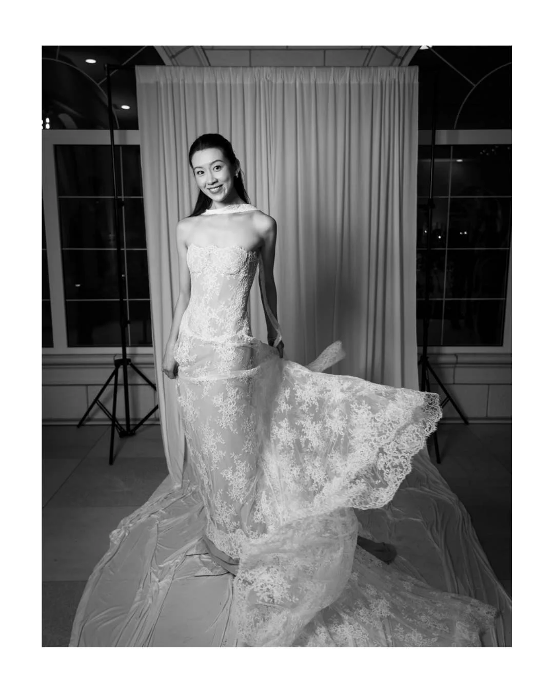 a bride poses for a black and white portrait in front of a draped backdrop and stone arches.