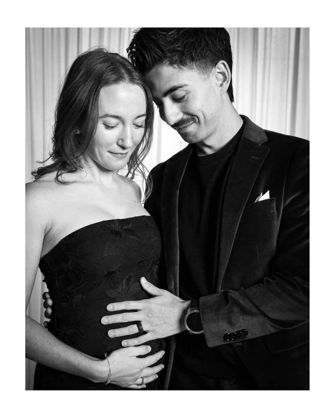 Expecting couple sharing a tender moment, his hand on her belly, in a wedding guest portrait