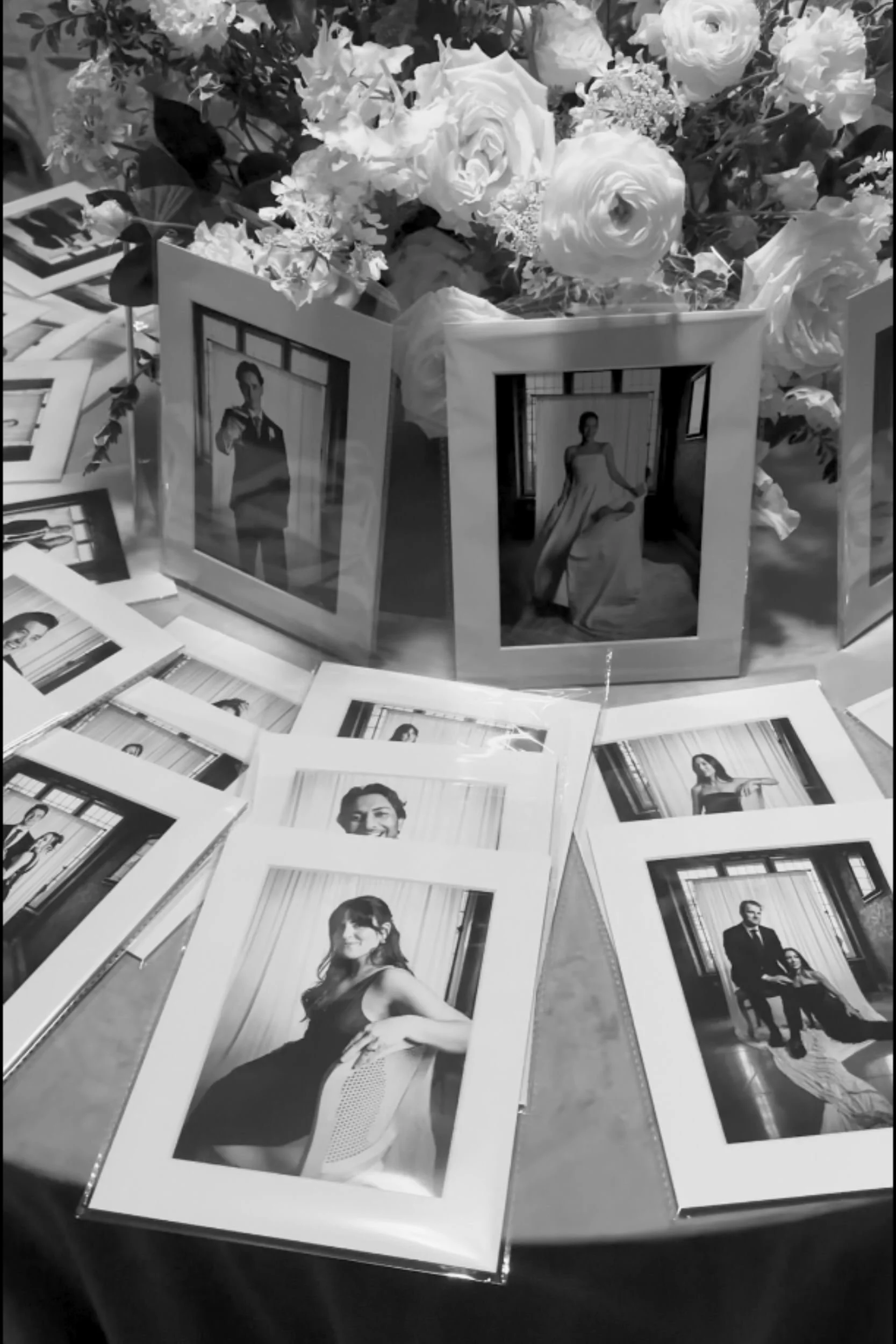 Black and white 8x10 matted guest portraits displayed among white flowers as wedding favours