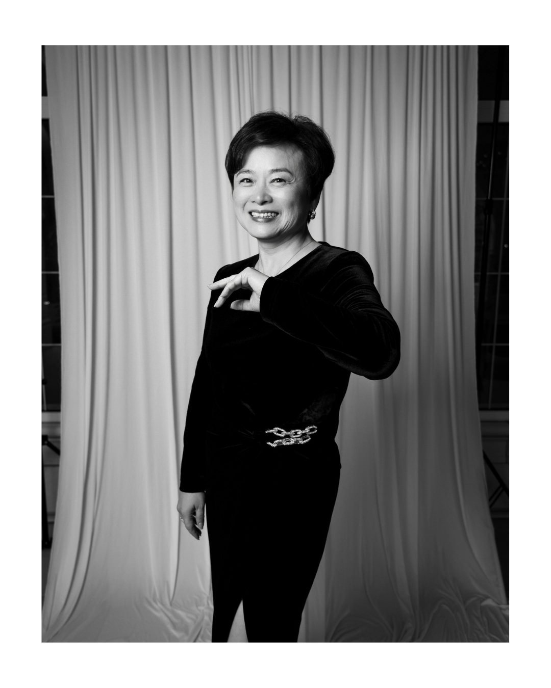 Black and white portrait of a smiling woman with short hair in a dark dress in front of a draped backdrop