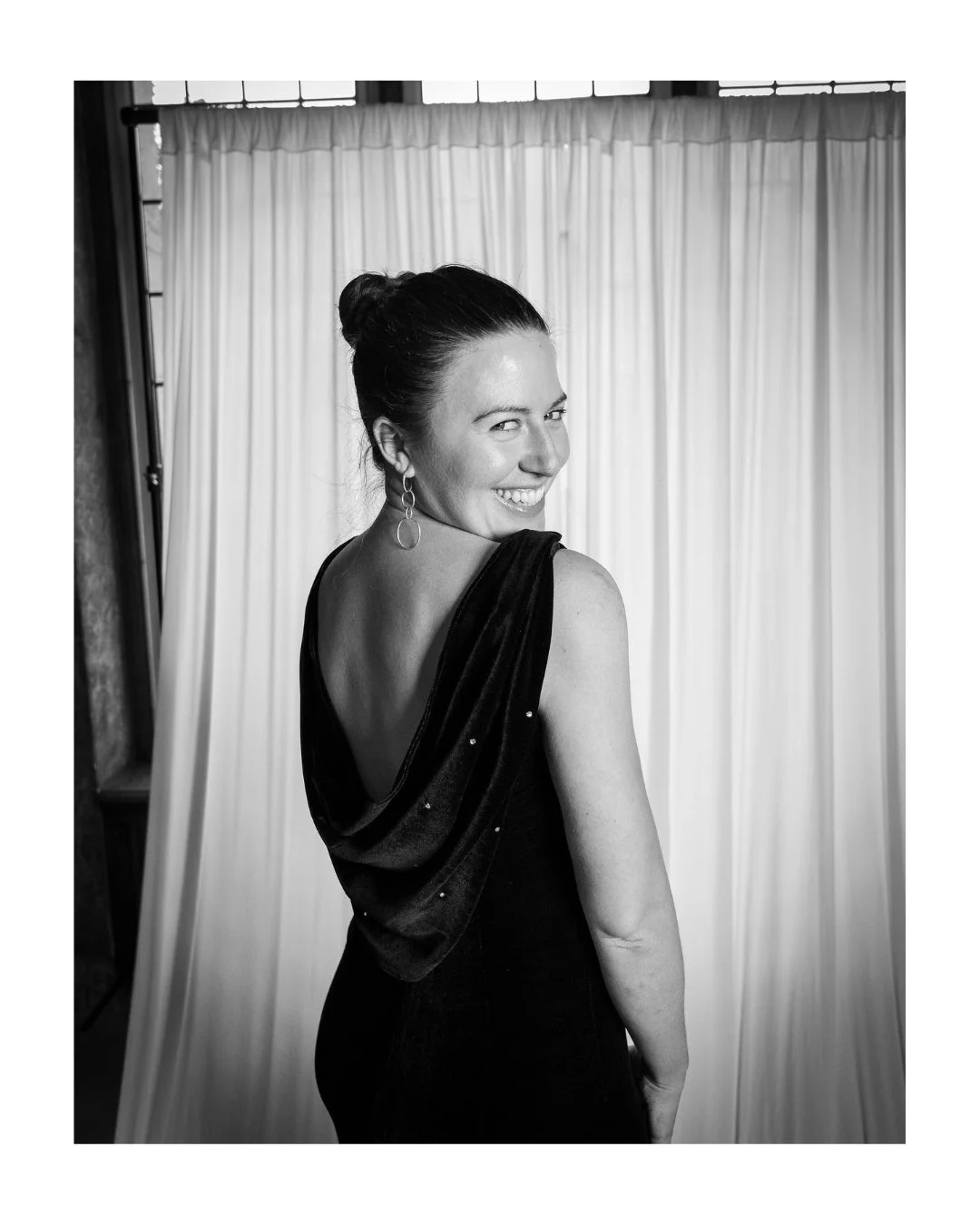 Black and white portrait of a smiling woman in an elegant black dress in front of a draped backdrop