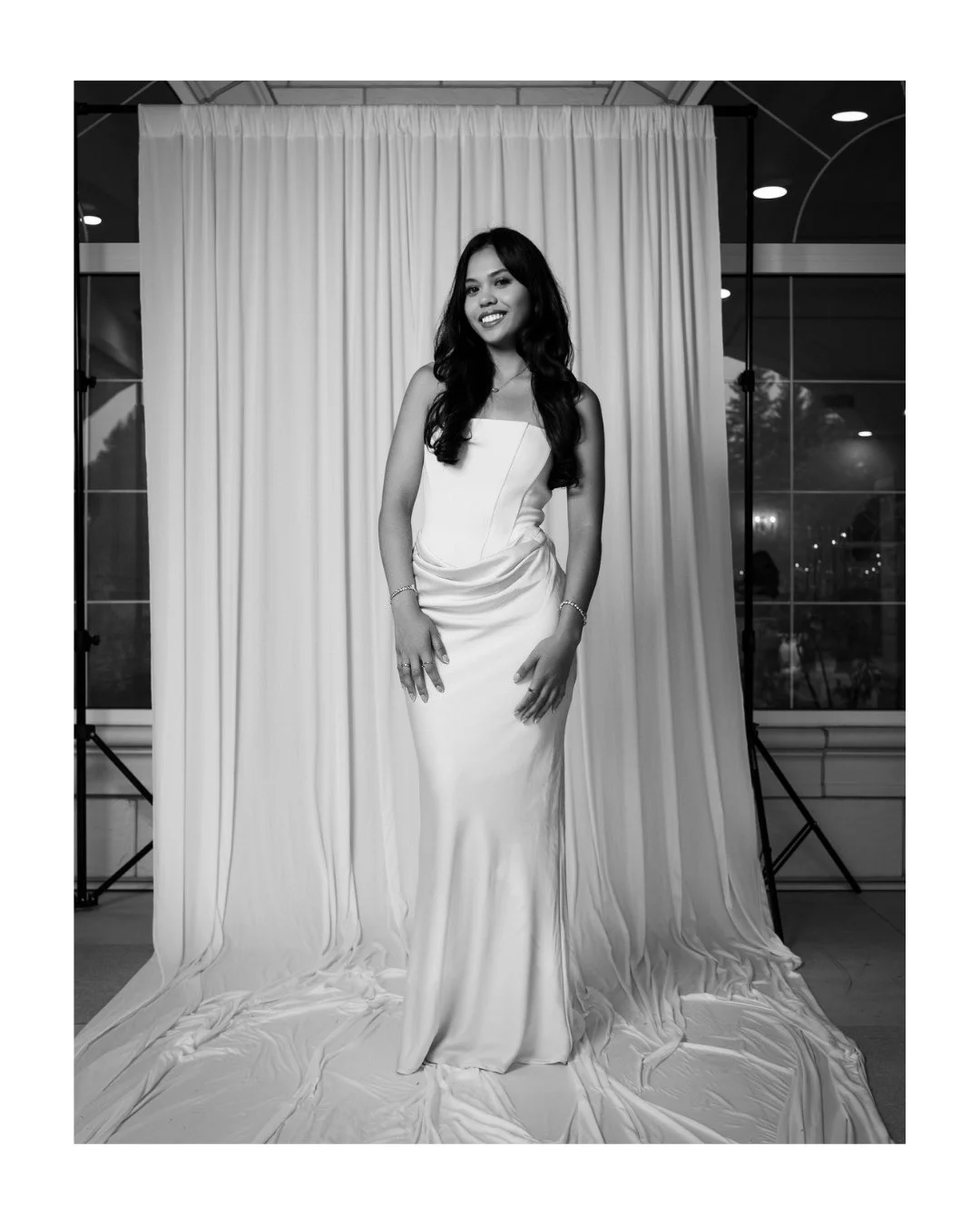 Smiling woman in a strapless floor-length satin gown in front of a white draped backdrop