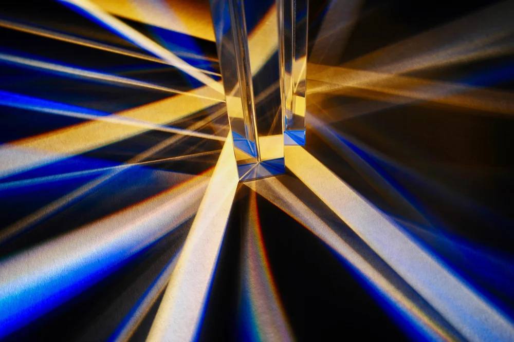 Light passing through two glass prisms and splitting into beams of blue and gold.