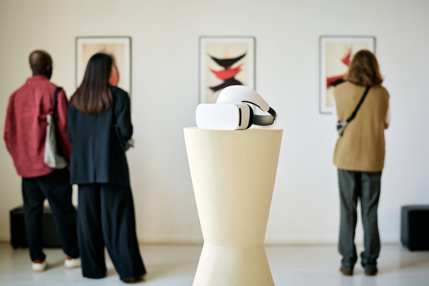 Visitors look at framed art in a gallery while a virtual reality headset rests on a pedestal