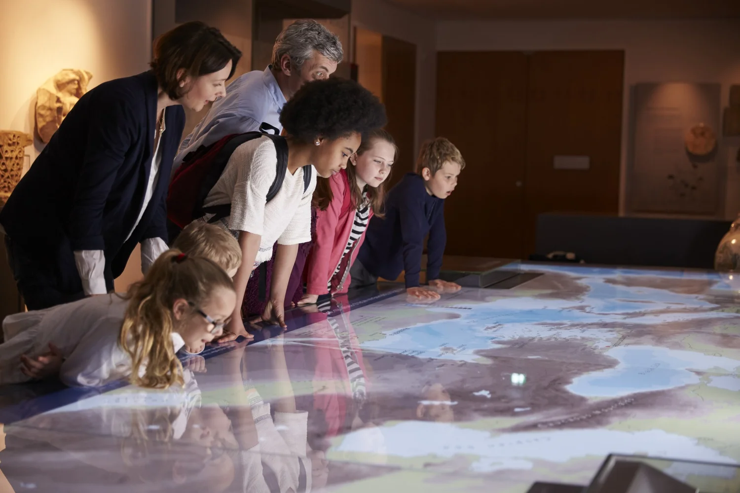 Children and adults lean over a lit map table in a museum