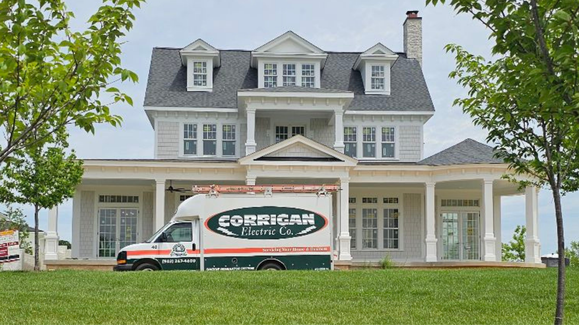 A large modern house with white siding and multiple windows, surrounded by green grass and trees, with a Corigan Electric Co. van parked in front.