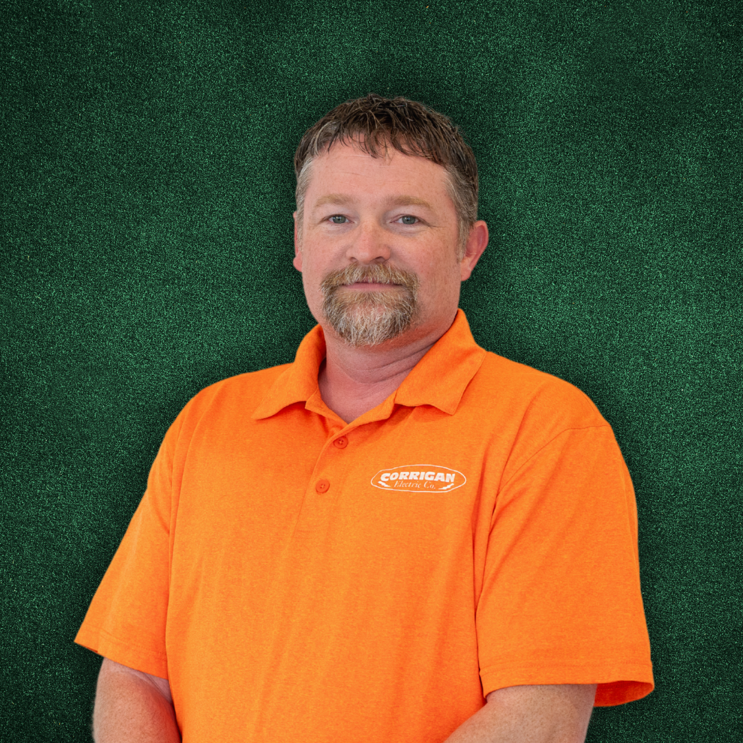 A man with short brown hair and a beard, wearing an orange polo shirt with a company logo, standing against a green textured background.