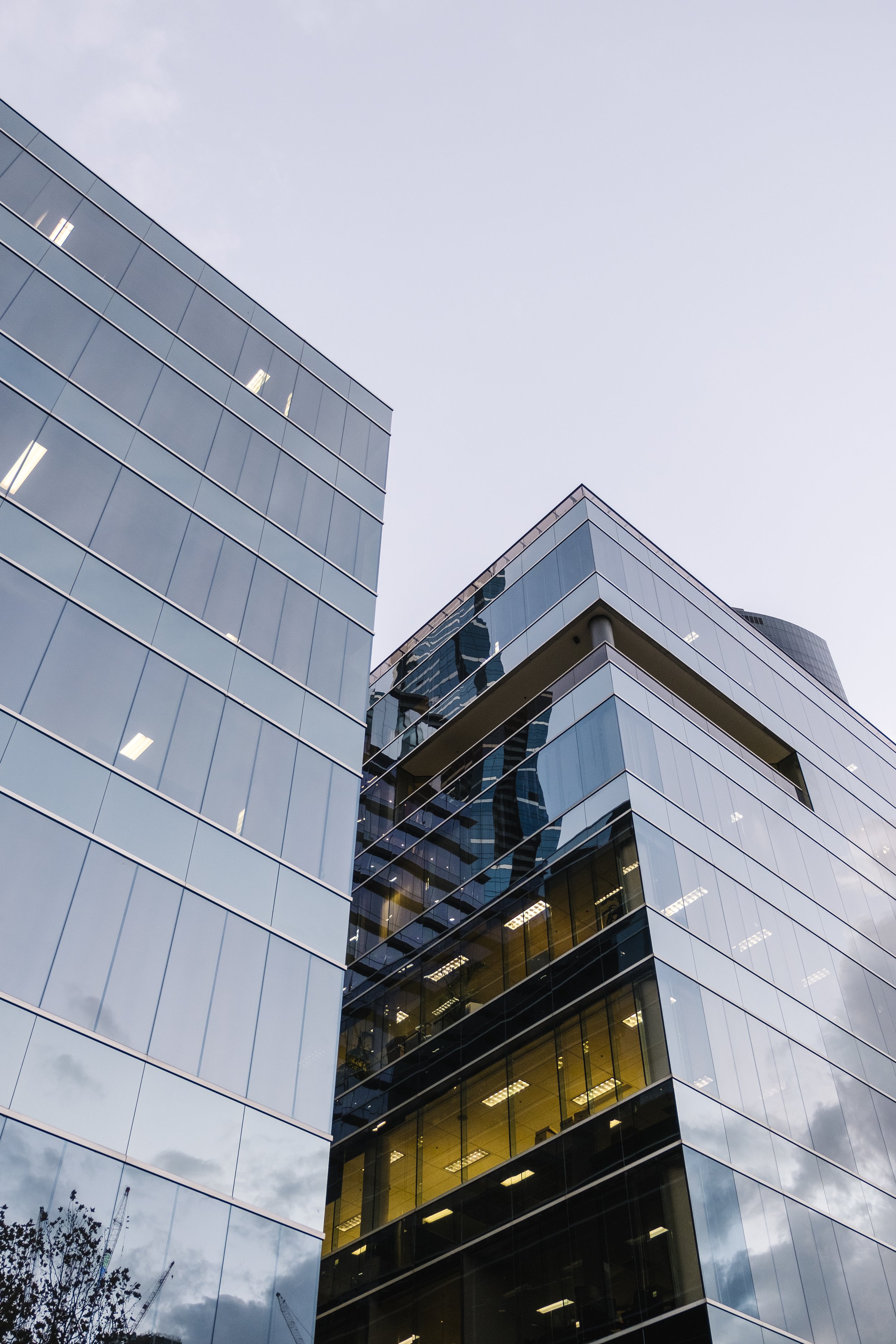 Tall modern glass office buildings with reflective windows under a cloudy sky.