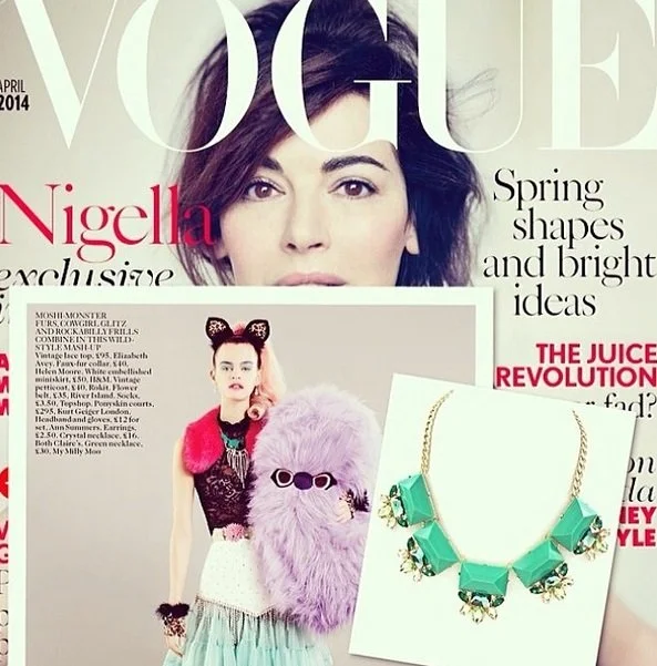 Cover of Vogue magazine featuring a woman with dark hair, and a smaller fashion image of a woman in colorful clothing holding a pink fur bag and wearing a green necklace with geometric green stones.