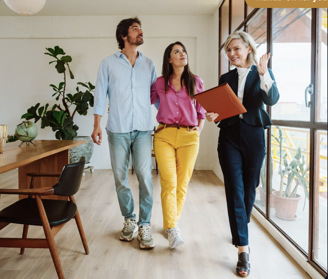 Three people, two women and one man, walking and talking inside a bright office space with large windows and indoor plants, led by a woman holding a folder.