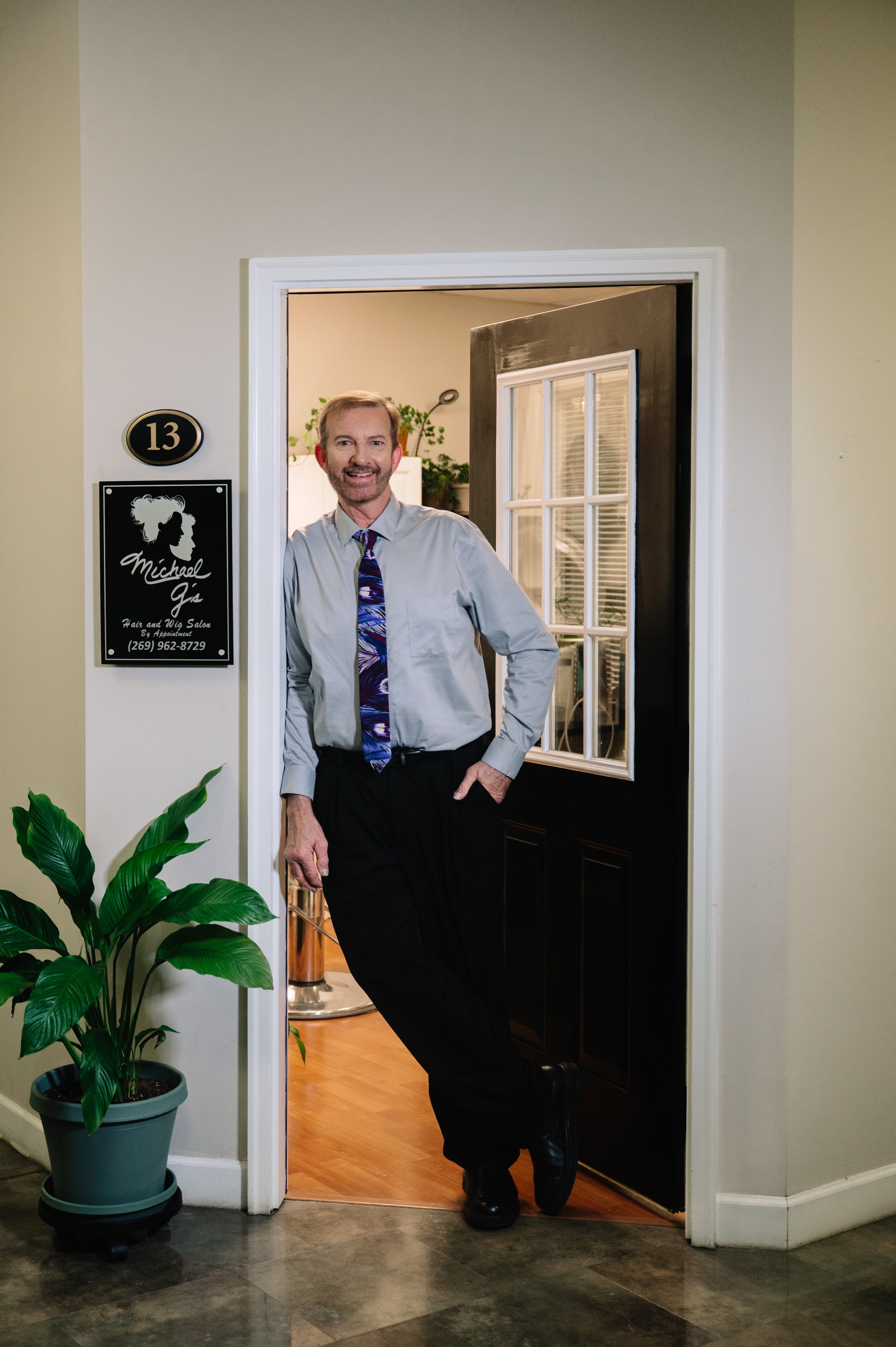 Ron Giacobassi leans in the doorway of his studio next to the sign that reads Michael G's Salon and Wig Studio