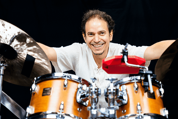 Happy man behind a drum set with cymbals, playing drums with a smile.
