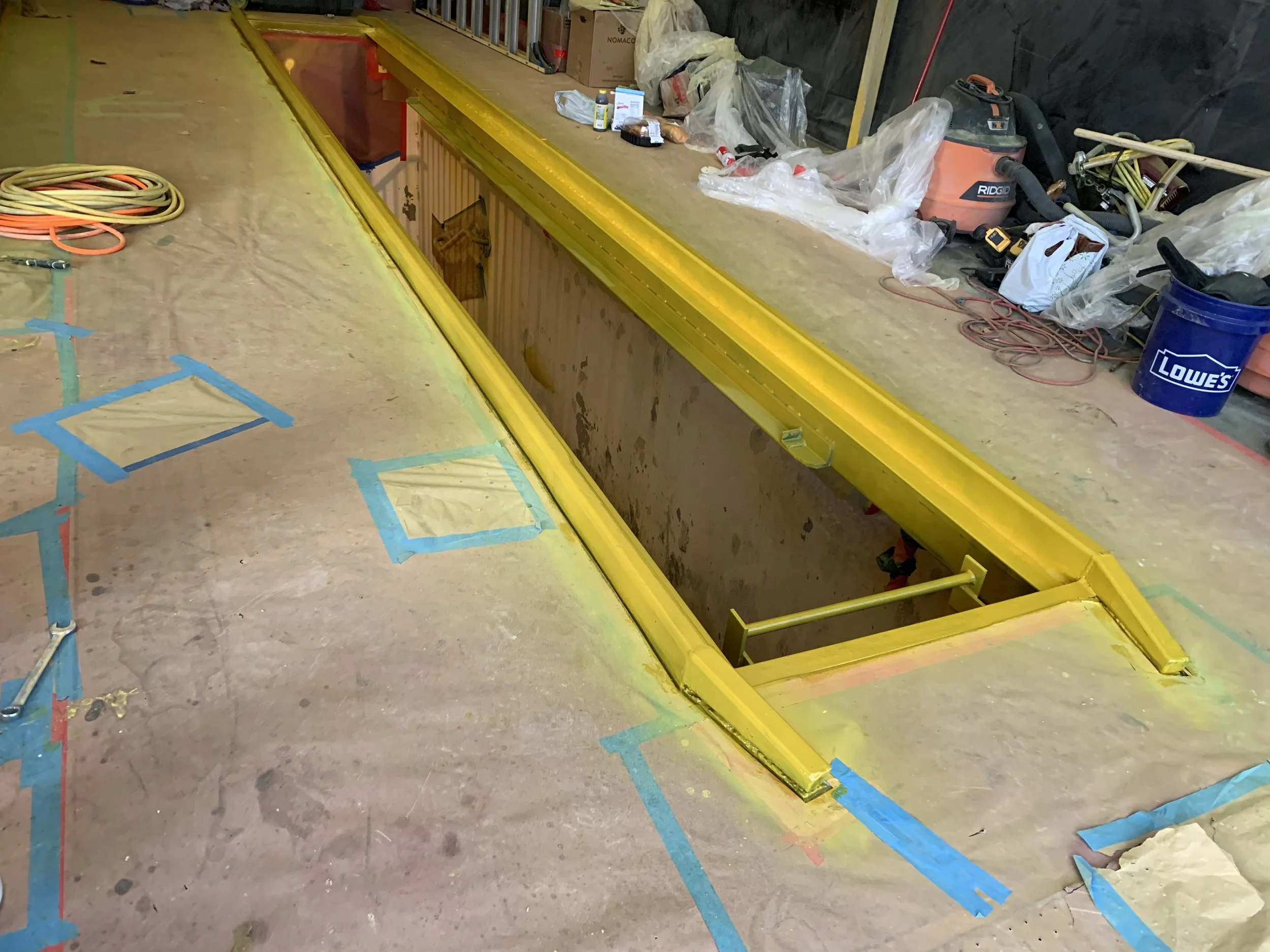Steel pit frame coated safety yellow with surrounding floor masked off