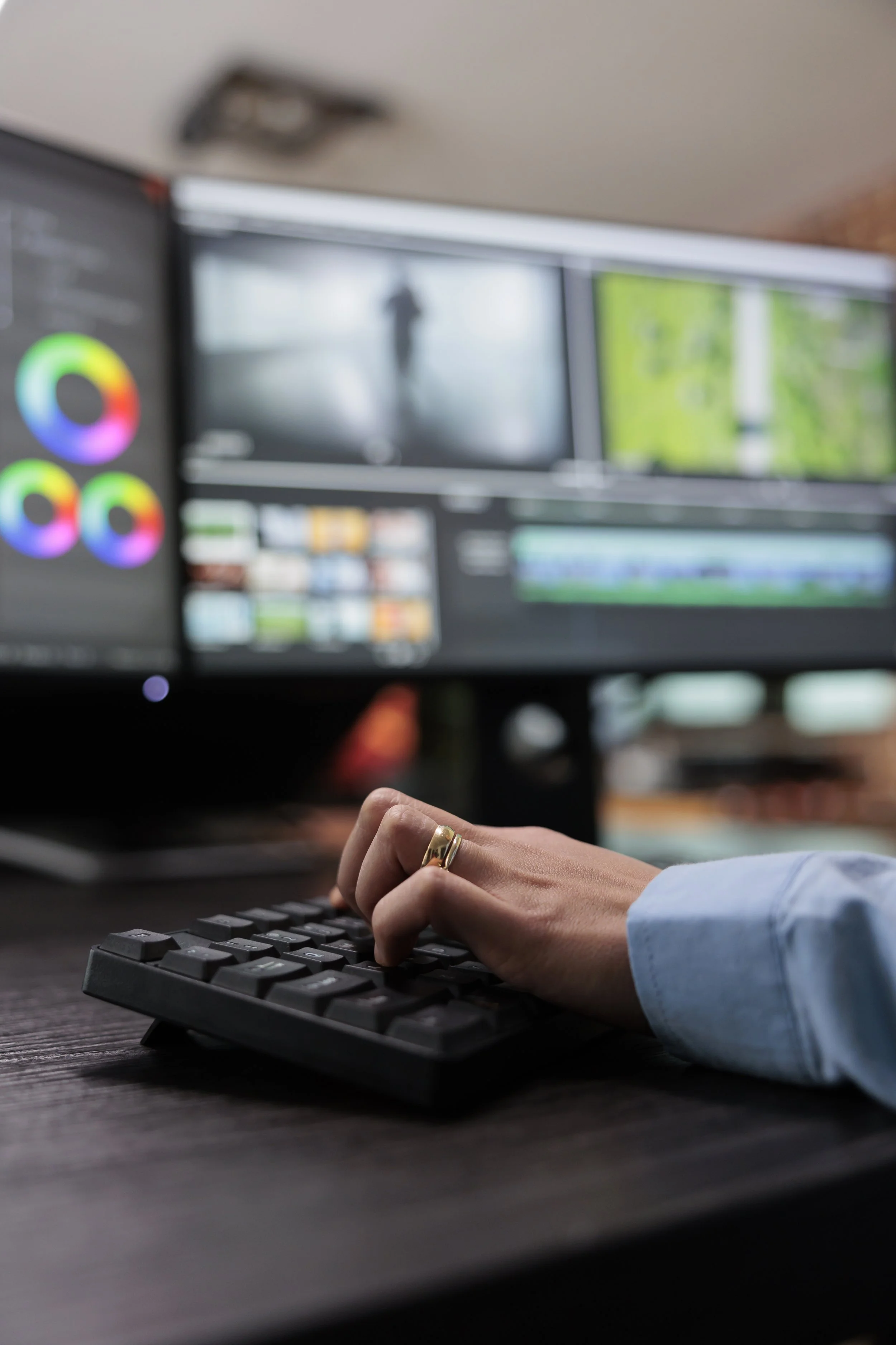 Person typing on a keyboard with multiple screens displaying video editing software in the background.