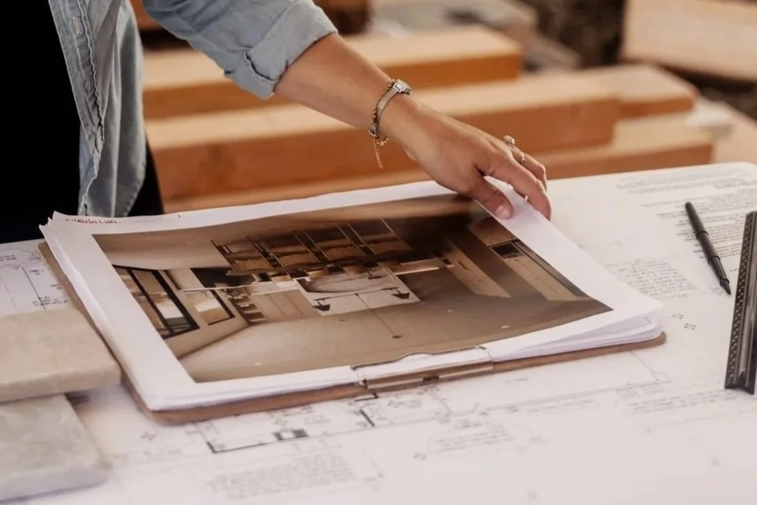 Person reviewing architectural plans and a photograph of an interior space at a workspace