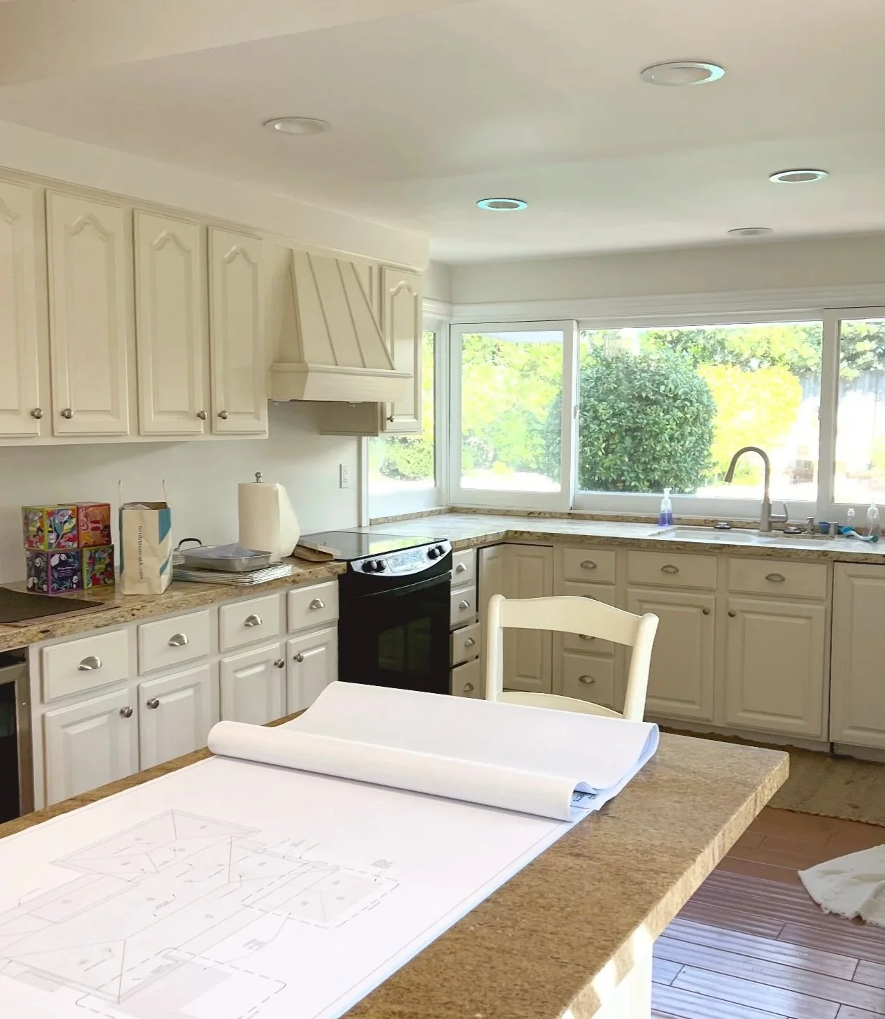 Westlake Residence kitchen before renovation, showing traditional white cabinetry, granite countertops, a black range and a large garden-facing window.