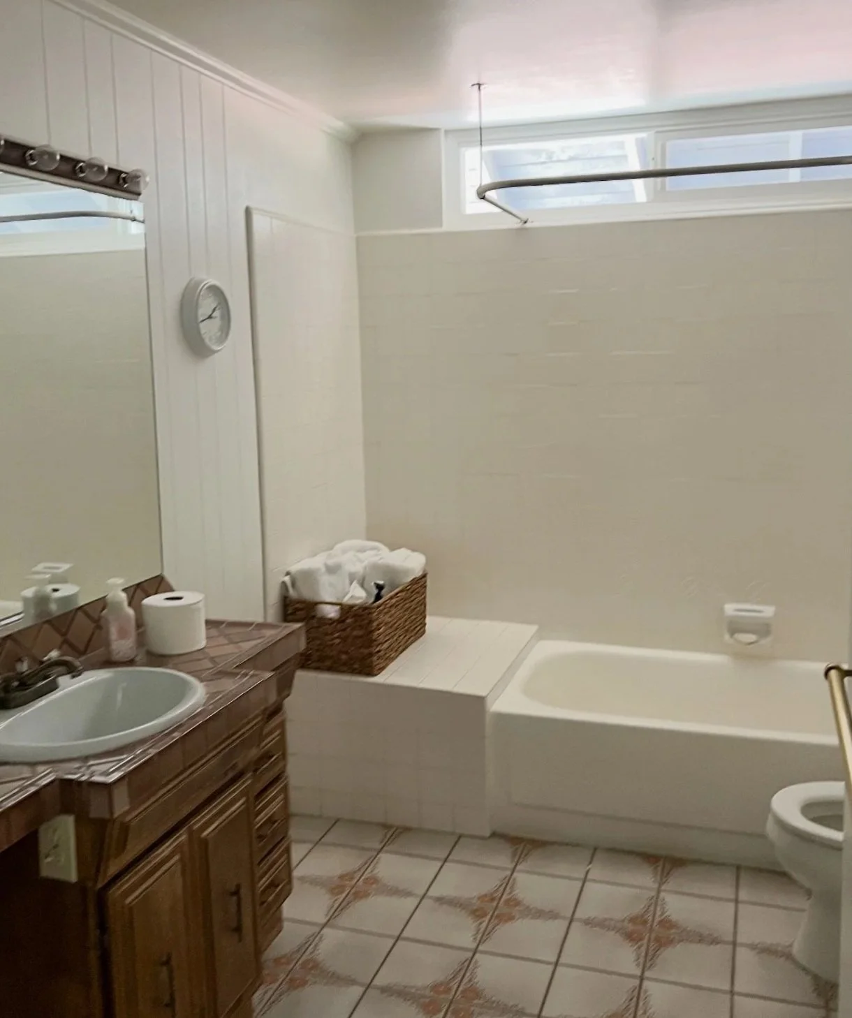 Original Westlake Residence bathroom before renovation, featuring a tiled floor, compact vanity, bathtub and high window.