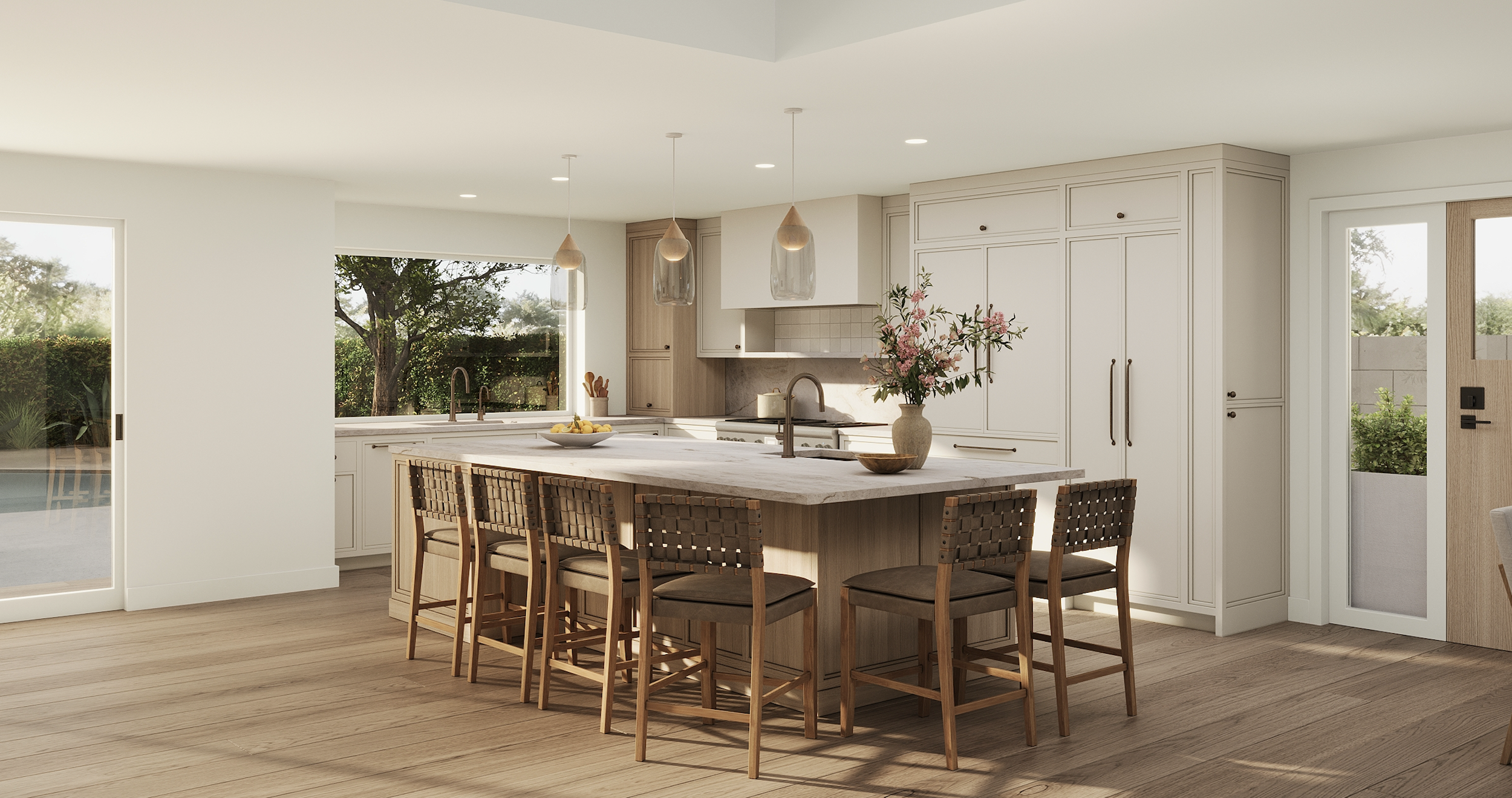 Modern kitchen with white cabinets, a large island with a marble countertop, hanging pendant lights, a vase with pink flowers, windows showing trees outside, and wood flooring.