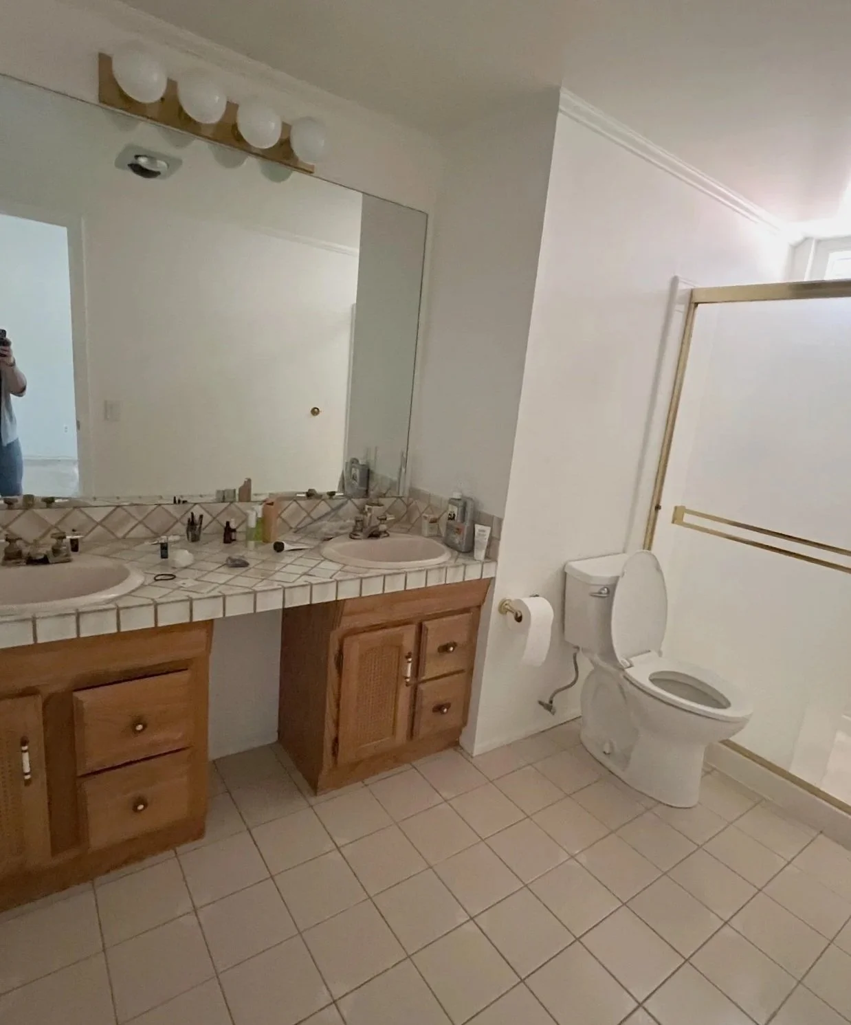 Before renovation of the Westlake Residence primary bathroom, showing the original wood double vanity, tiled countertop and enclosed shower.