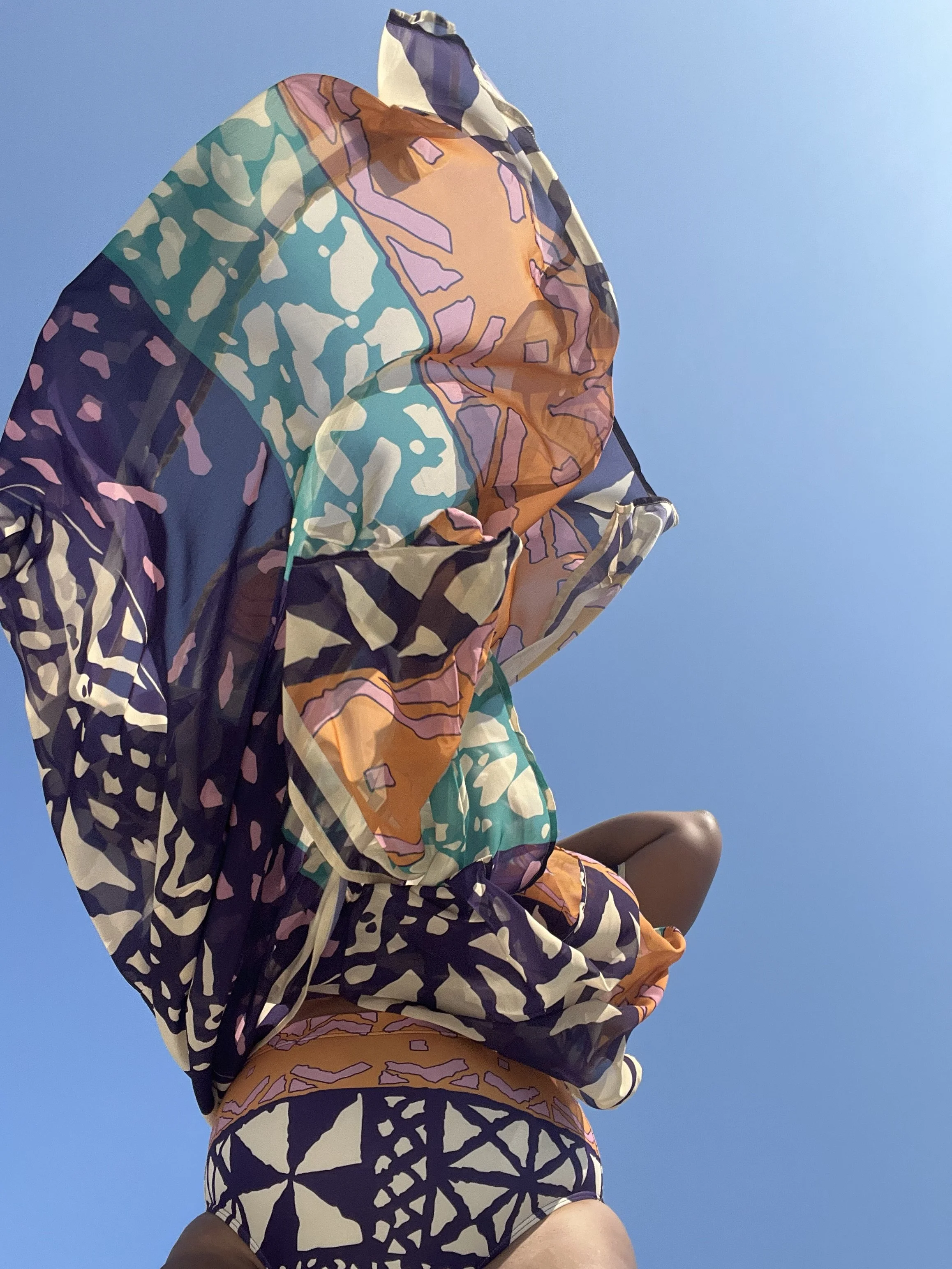 Vibes UnMatched founder wearing a colorful patterned wrap against a bright blue sky.