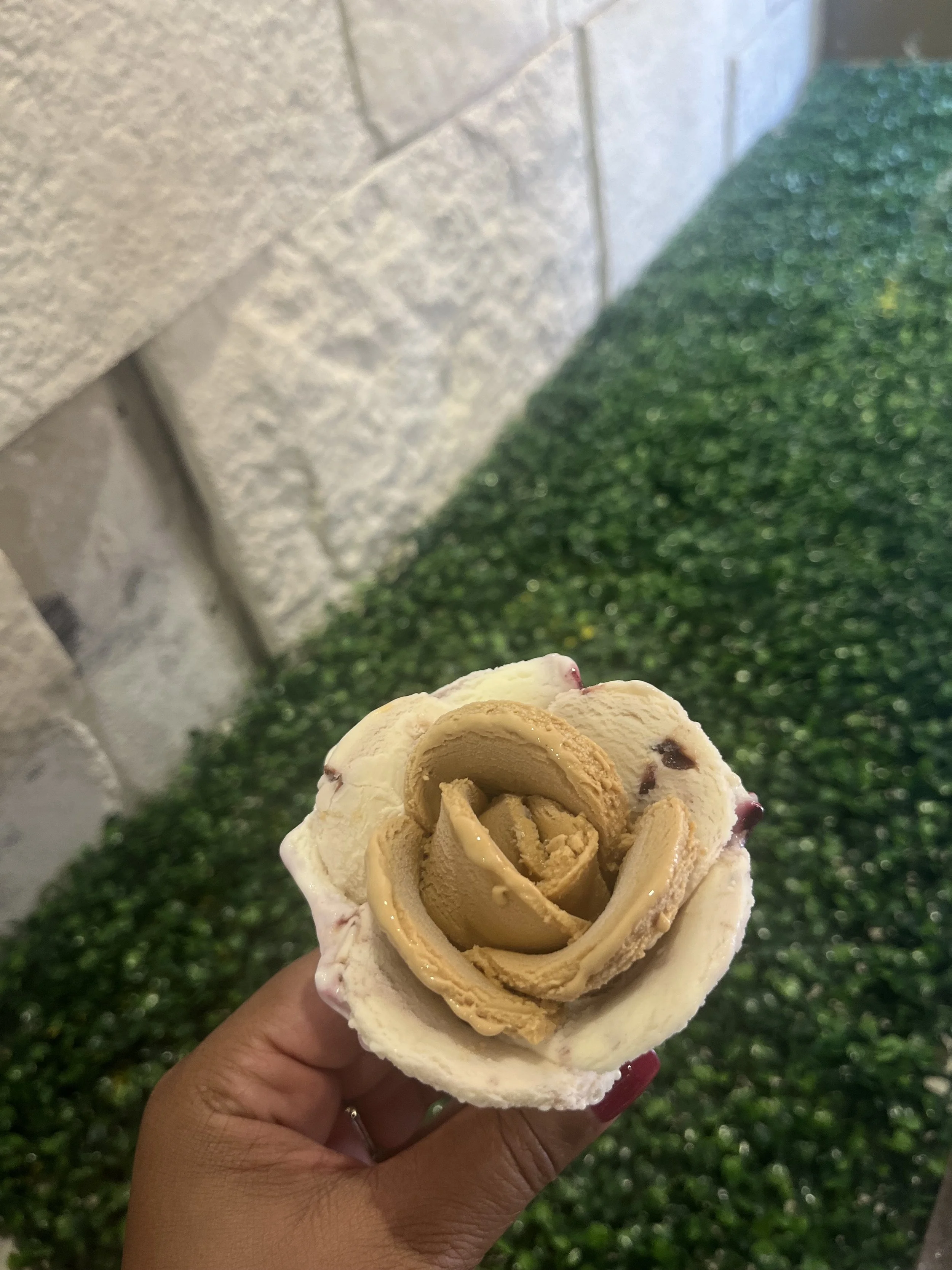 Hand holding a rose-shaped vanilla gelato cone outdoors.