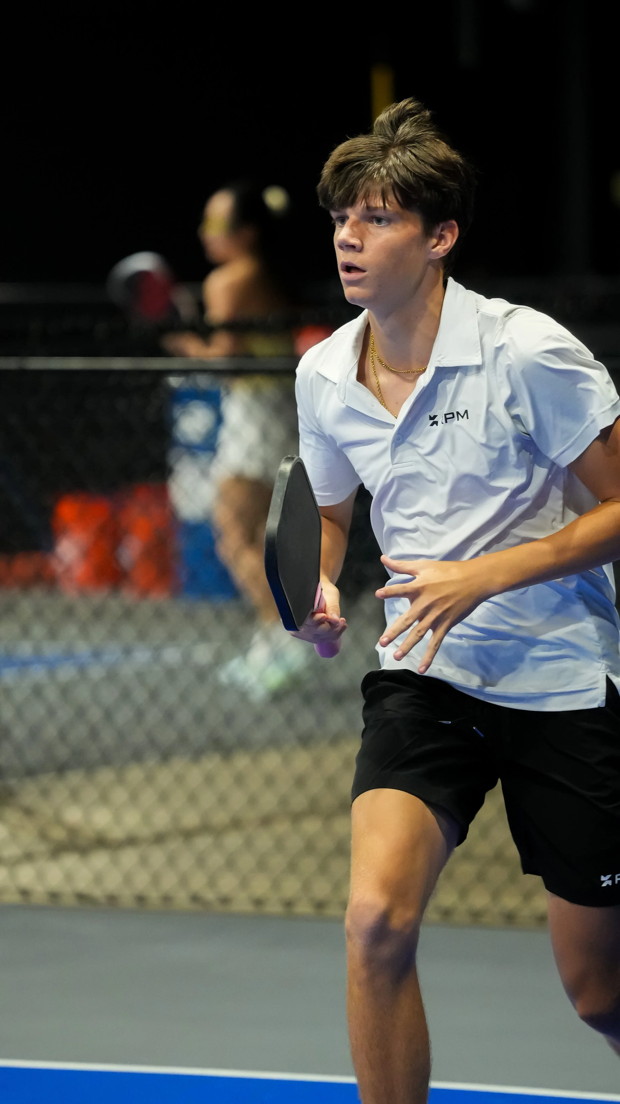 Young man playing ping pong, holding paddle, in an indoor sports facility.