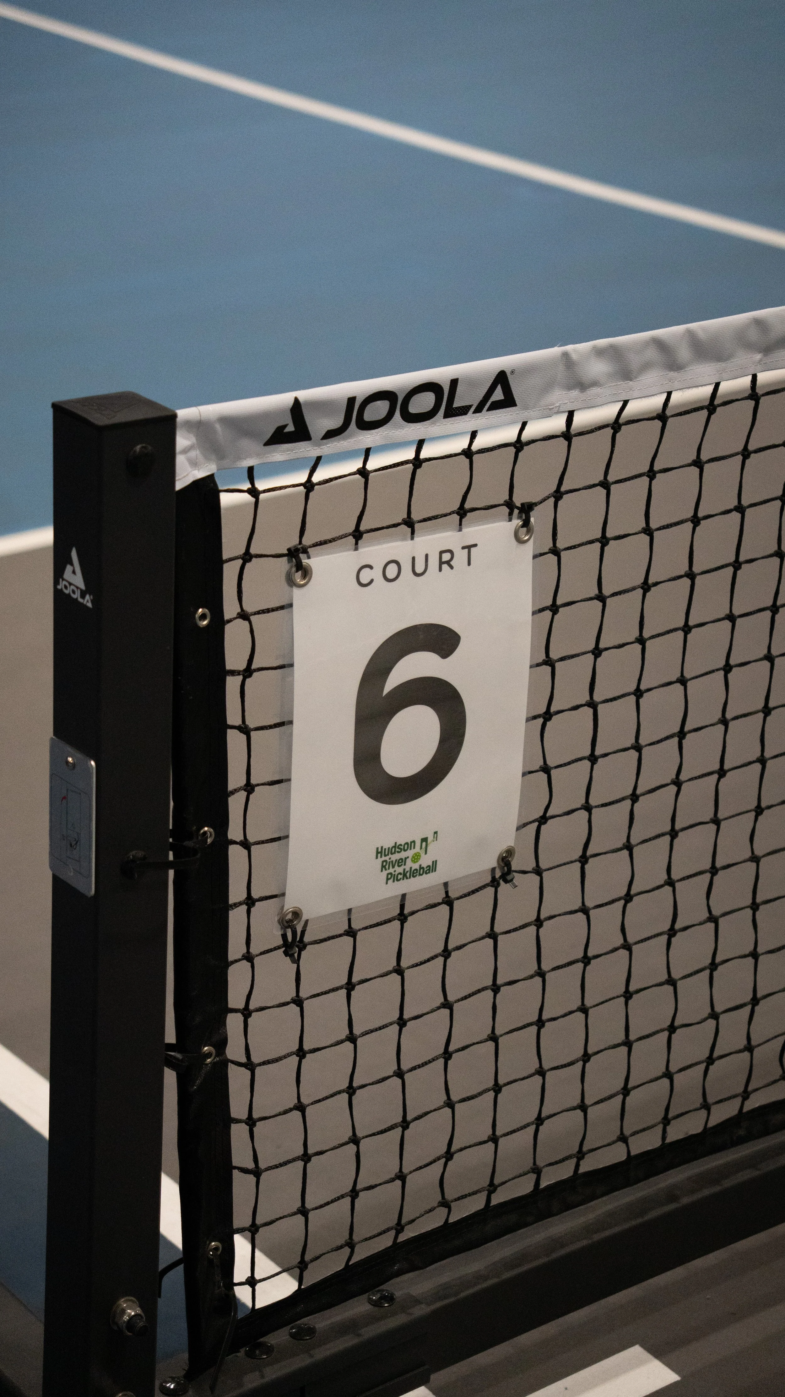 A volleyball net with a sign reading 'Court 6' and a logo for Hudson River Pickleball.